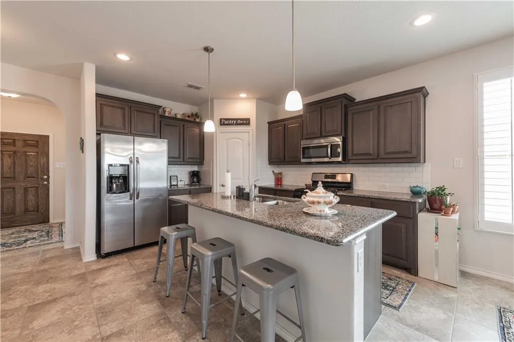 Modern kitchen featuring dark wood cabinetry, granite countertops, stainless steel appliances including a side-by-side refrigerator and built-in microwave, a large center island with seating for three, and pendant lighting