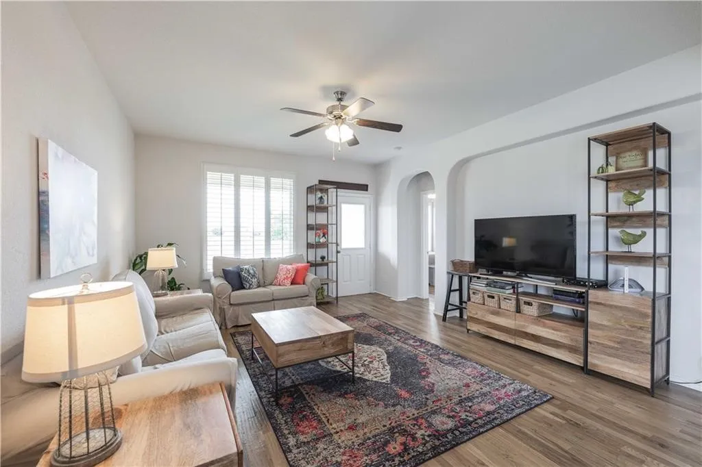 Spacious living area featuring wood-finish flooring, a ceiling fan, and white walls