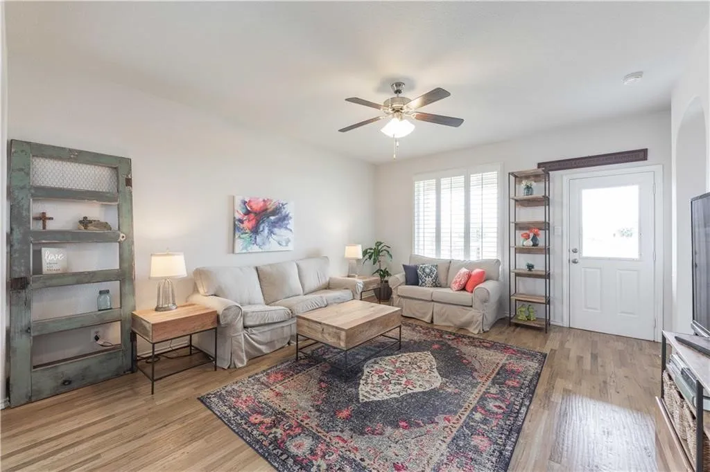 Spacious living area featuring wood-finish flooring, a ceiling fan, and window shutters
