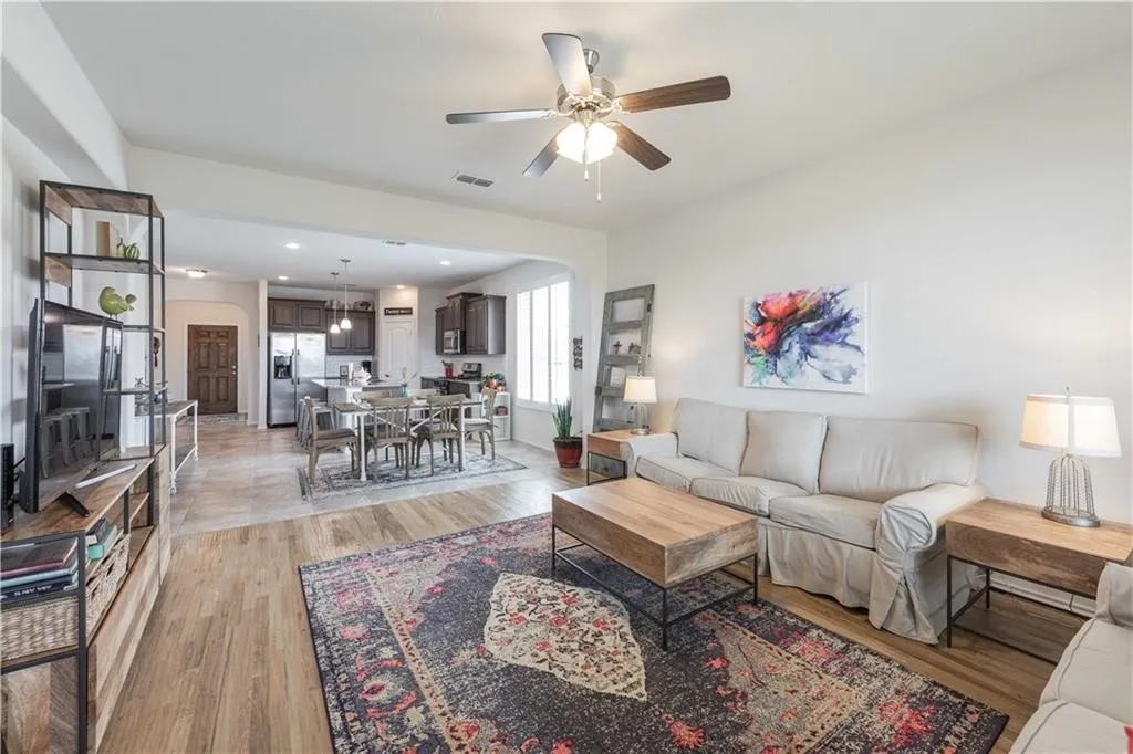 Open-concept living and dining area featuring wood-finish flooring throughout, a ceiling fan with integrated lighting, and abundant natural light from multiple windows