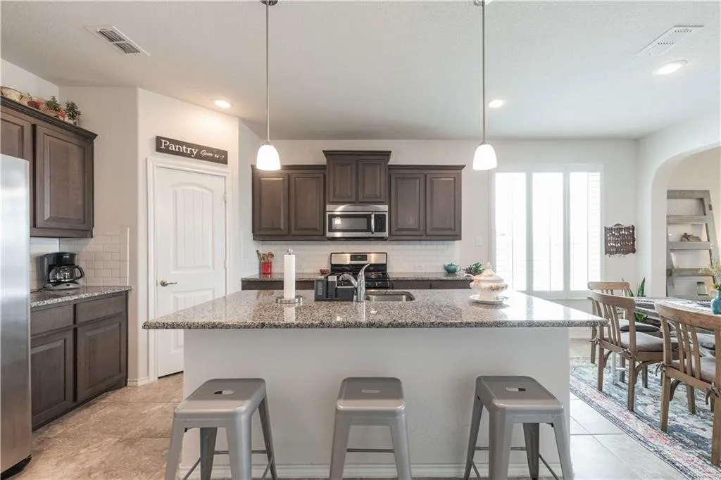 Chef's kitchen featuring dark wood cabinetry, stainless steel appliances, and a spacious granite-topped island with seating for three