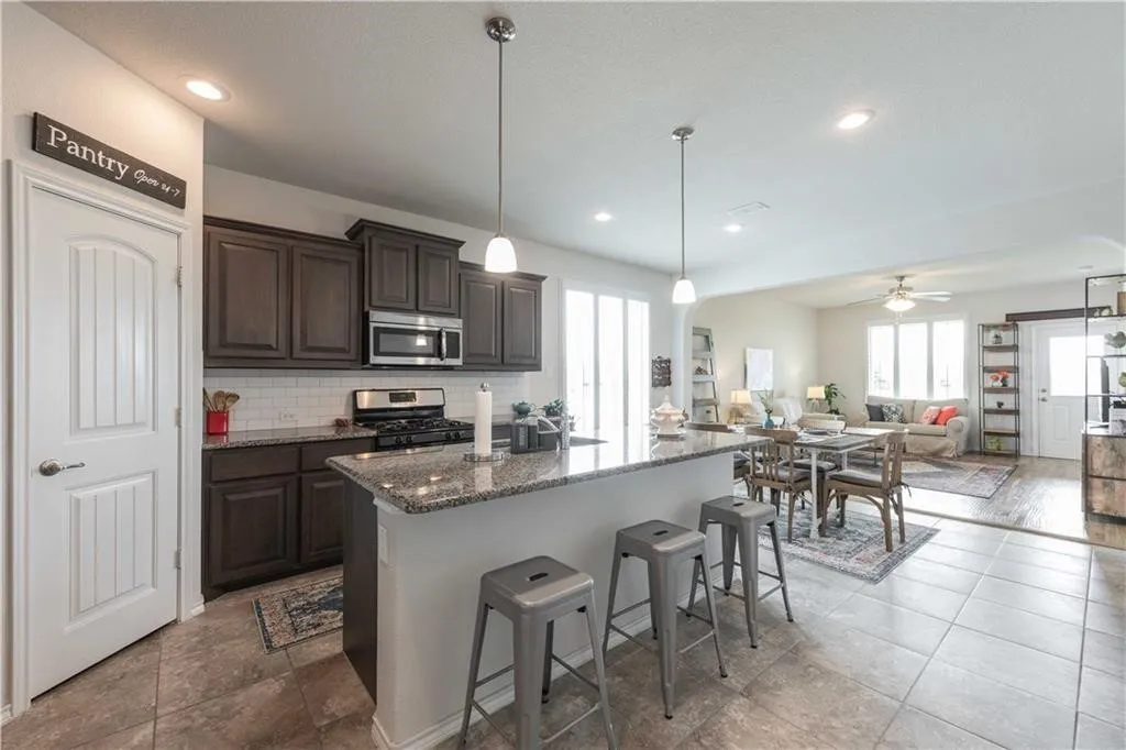 Open-concept kitchen and living area featuring dark wood cabinetry, stainless steel appliances, granite countertops, and a large island with seating