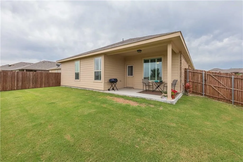 Manicured lawn with a covered concrete patio, privacy fencing, and exterior brick accents