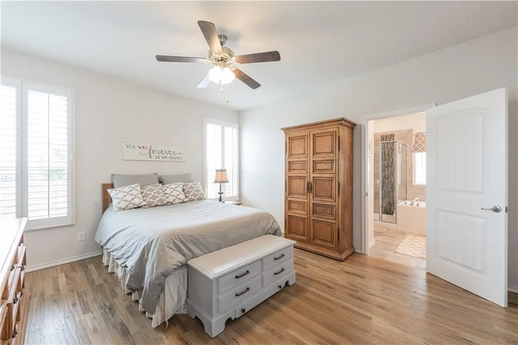 Spacious primary bedroom with hardwood flooring, ceiling fan with integrated lighting, and abundant natural light from dual windows