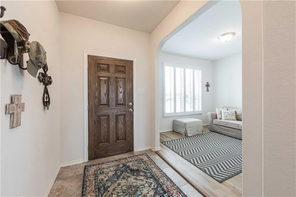 Archway entry leading to an interior space with wood-finish flooring, a window featuring plantation shutters, and an overhead light fixture