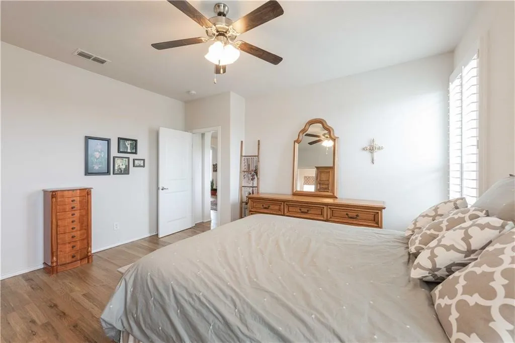 Spacious primary bedroom featuring hardwood flooring, ceiling fan with integrated lighting, and abundant natural light from multiple windows