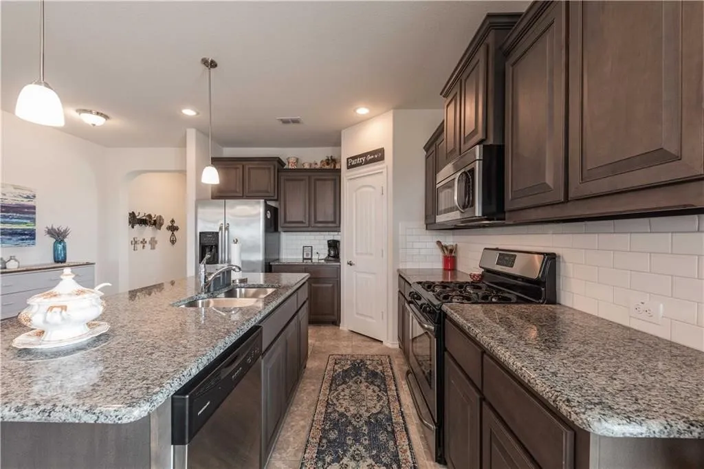 Kitchen featuring granite countertops, dark wood-finish cabinetry, stainless steel appliances, a subway tile backsplash, and recessed lighting