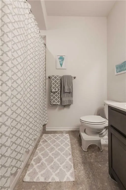 Contemporary bathroom featuring a geometric-patterned shower curtain, dual towel bars with coordinating towels, white ceramic toilet, stone-finish flooring, and soft neutral wall tones
