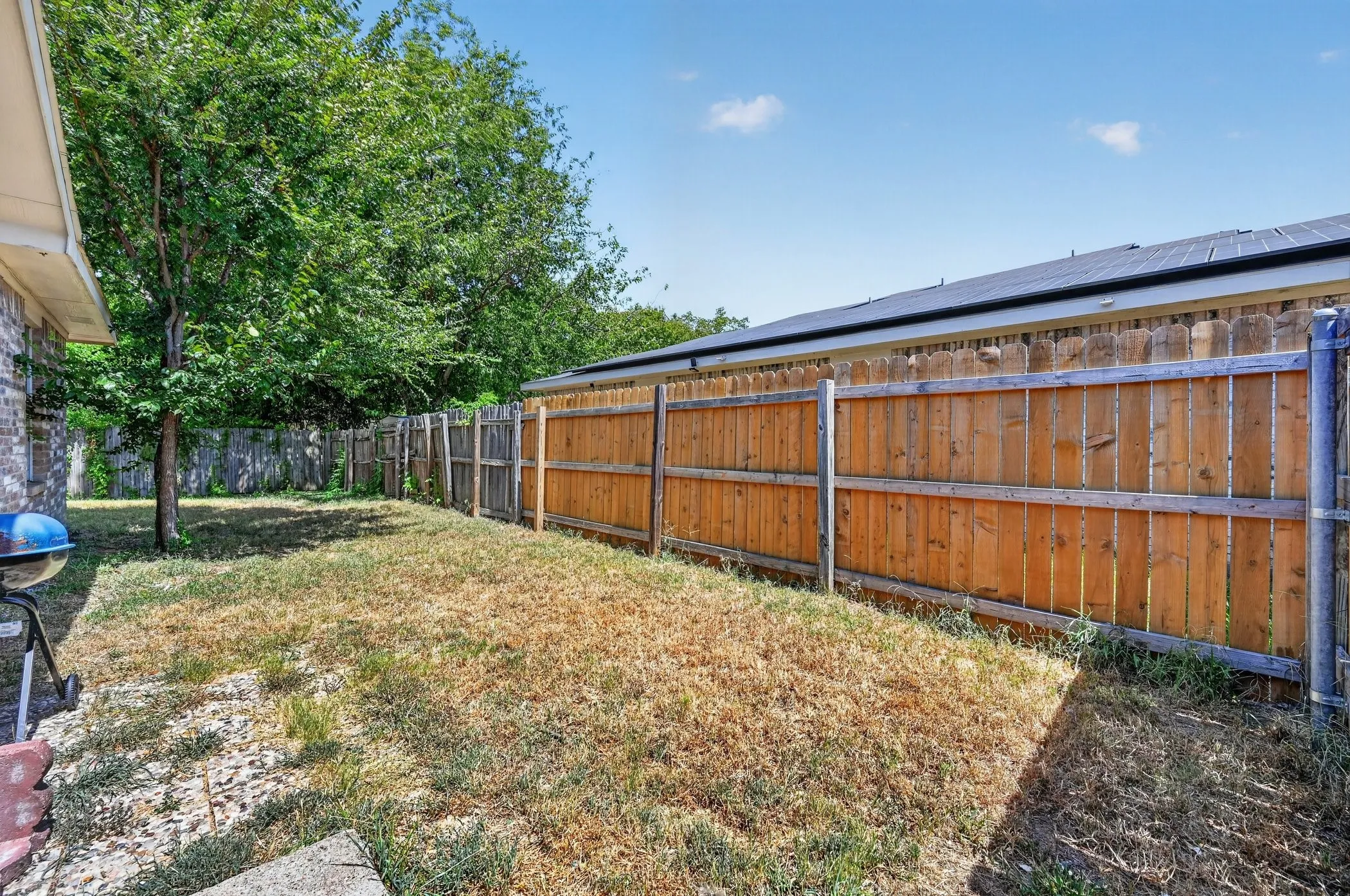 Expansive backyard with a wood privacy fence, mature trees, and solar panels visible on an adjacent structure