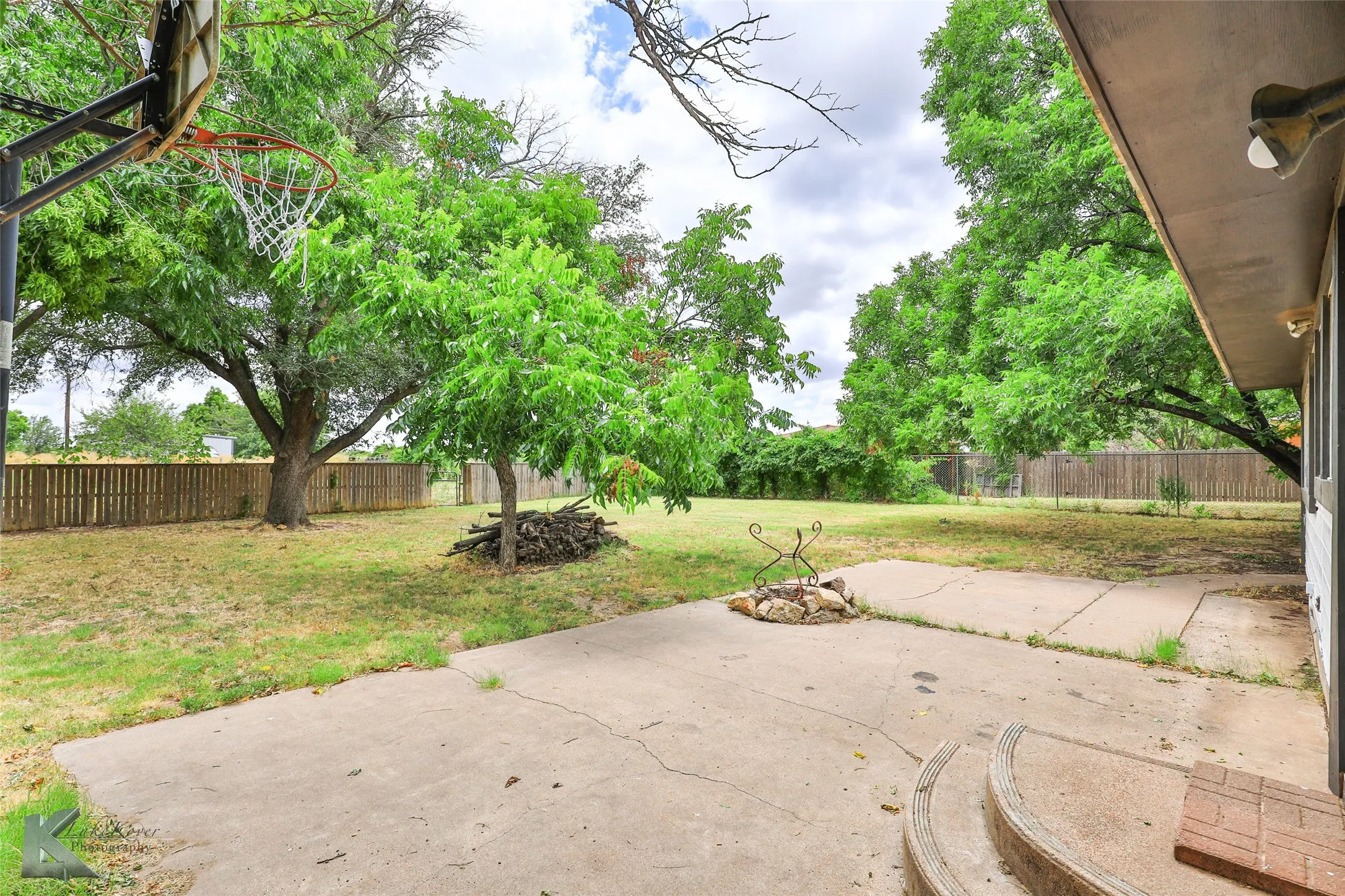 Expansive backyard featuring a mature tree canopy, level concrete patio, and wood-finish fencing throughout