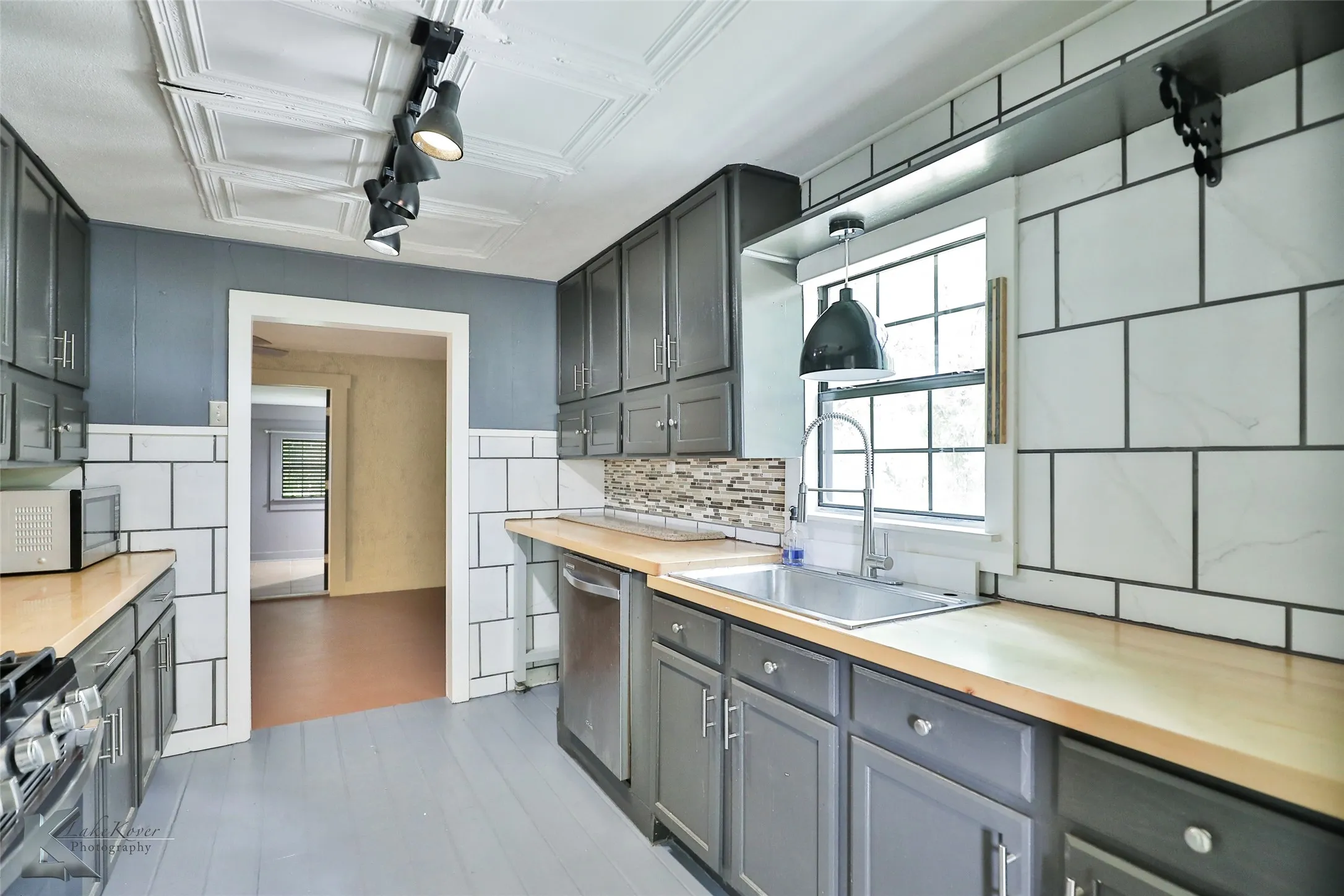 Galley kitchen featuring gray cabinetry with wood-finish countertops, subway tile backsplash, stainless steel appliances, and abundant natural light from large windows