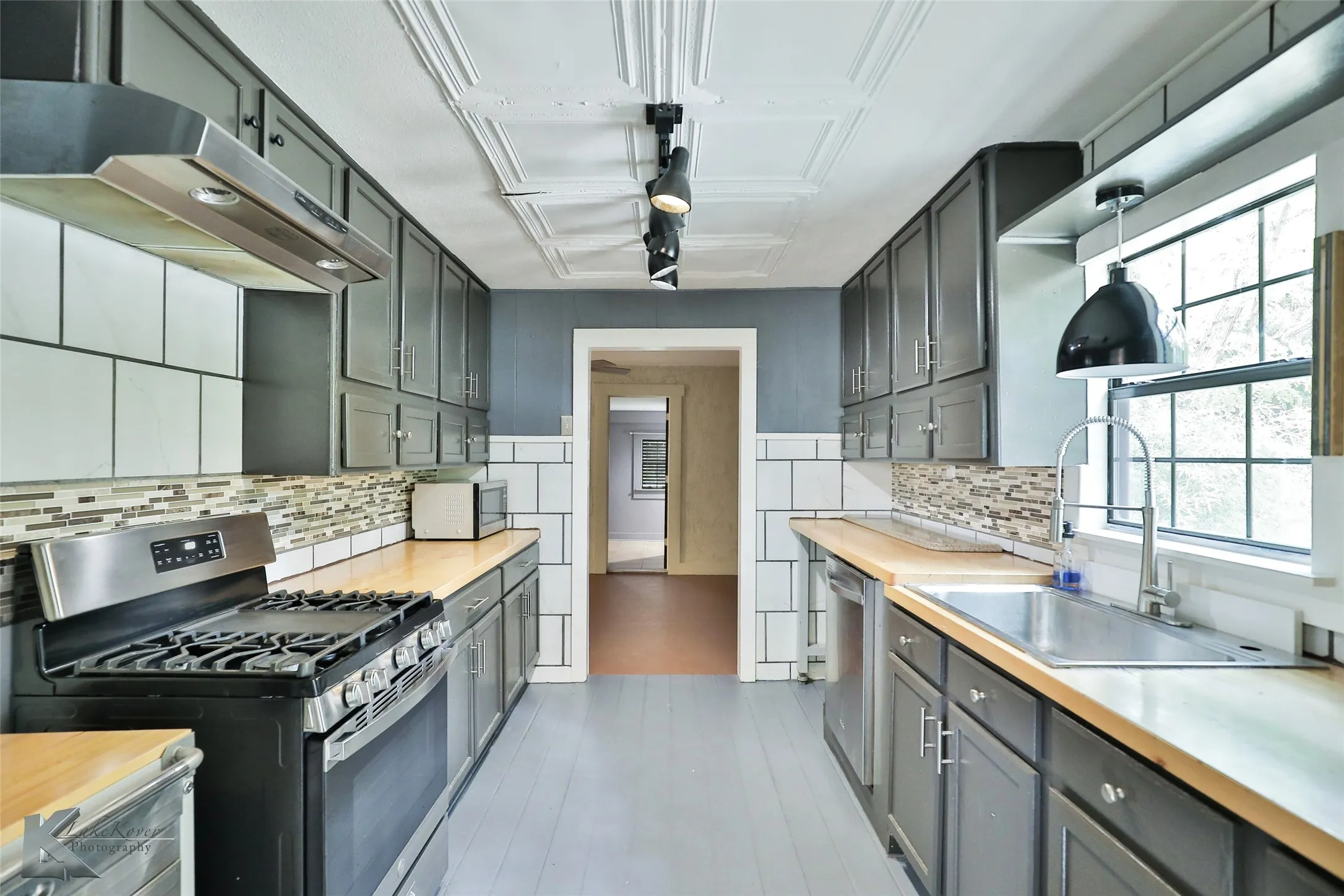 Galley kitchen featuring wood-finish countertops, stainless steel appliances, dark cabinetry, and a subway tile backsplash