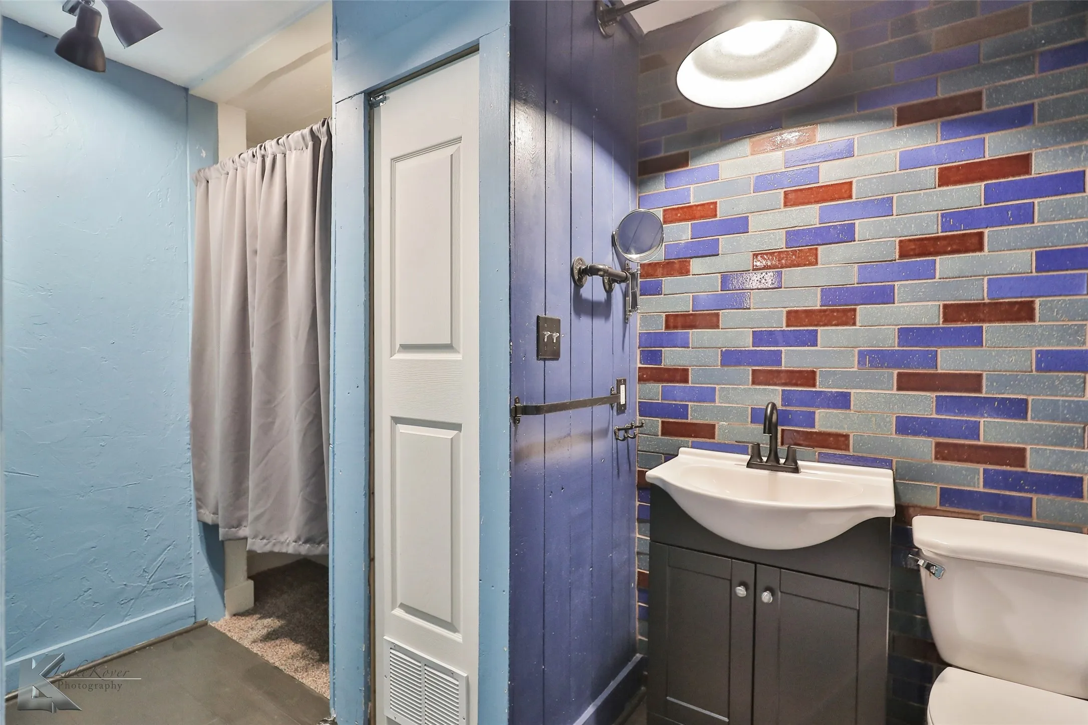 Master bathroom featuring a custom dark cabinetry vanity with integrated sink, colorful hand-laid tile backsplash in jewel tones and earth tones, recessed ceiling lighting, and a separate shower enclosure with glass partition and rainfall showerhead