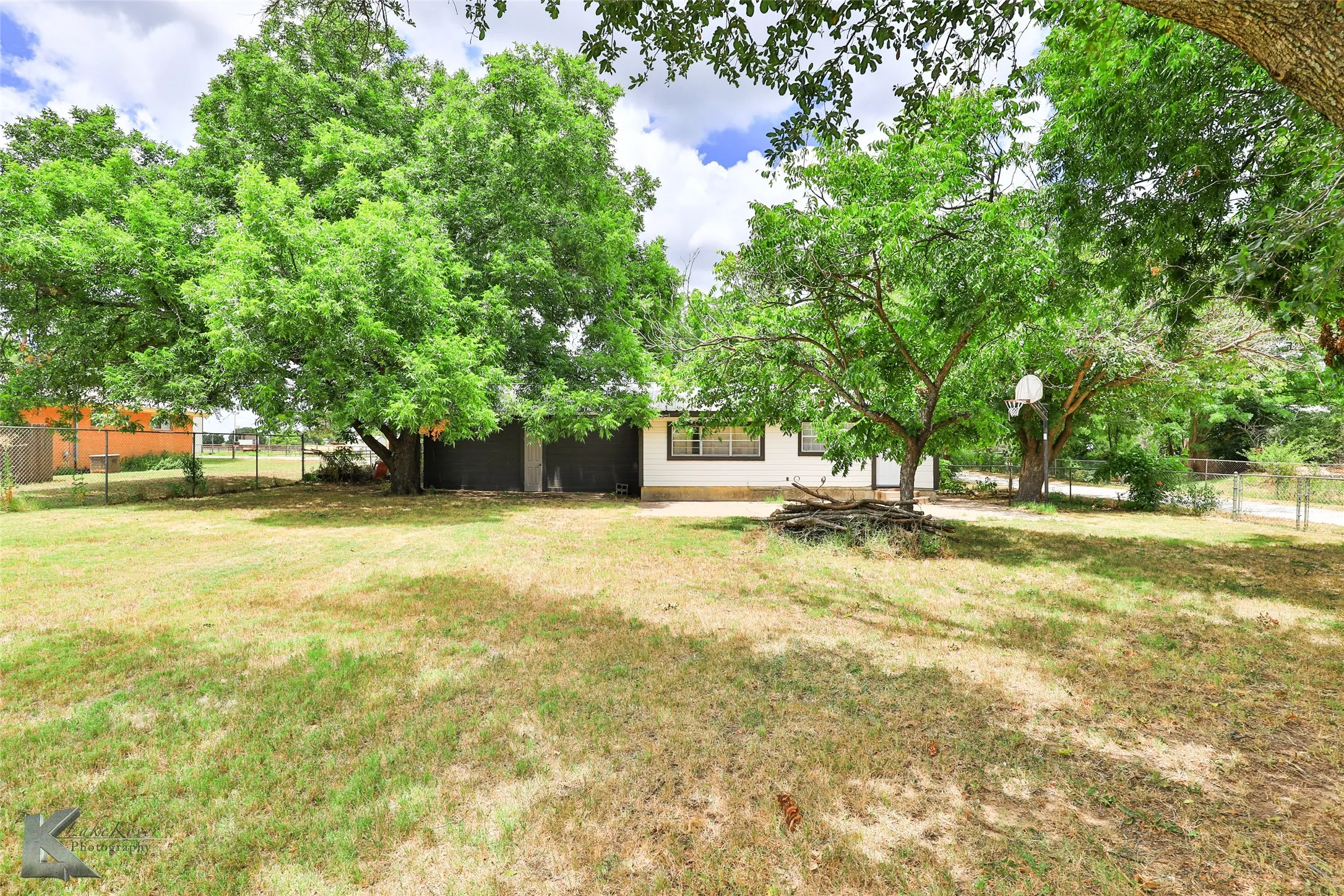 Expansive backyard with a generous lawn, mature trees, and chain-link fencing