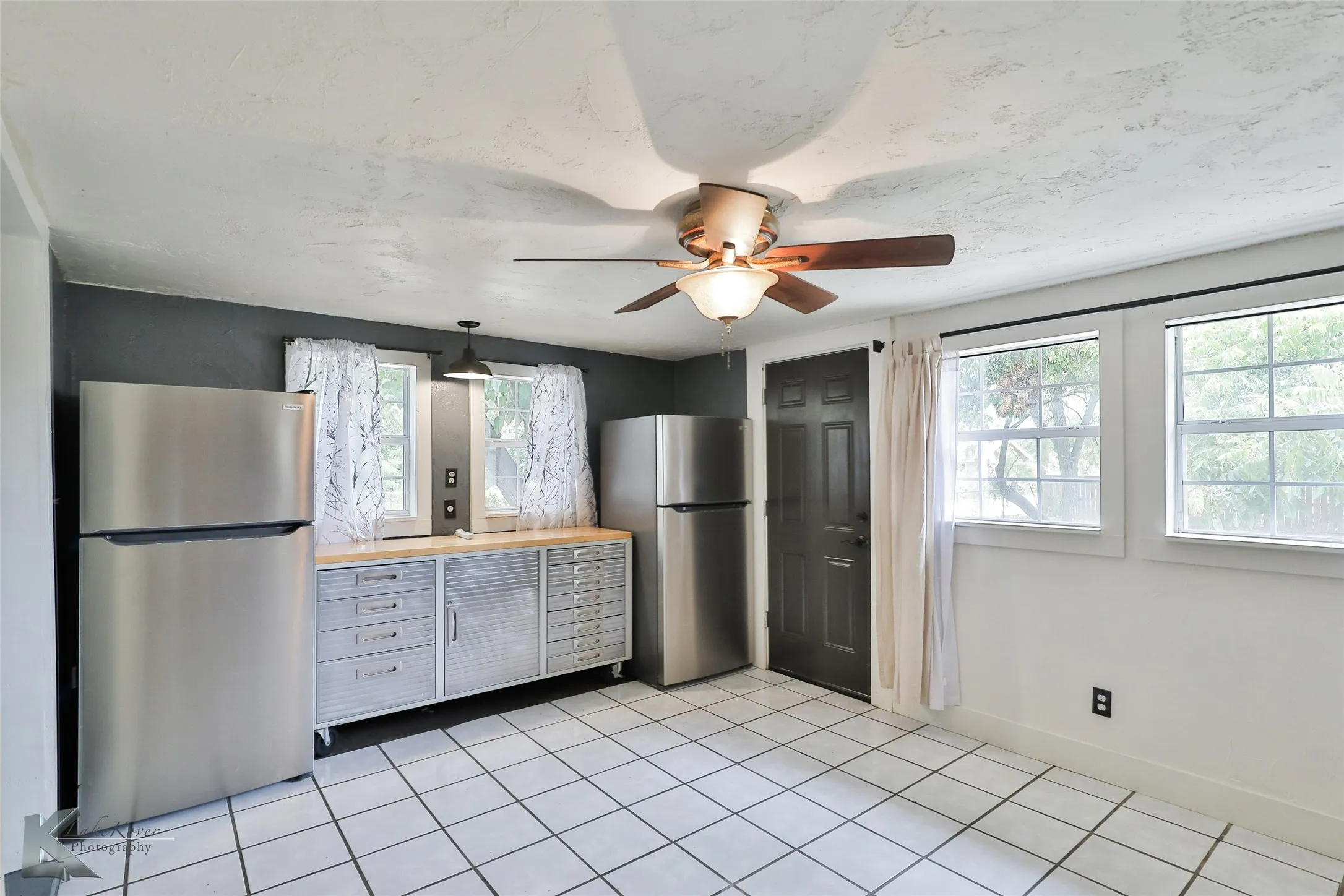 Spacious kitchen featuring stainless steel appliances, including a refrigerator and pantry-style storage, complemented by wood-finish cabinetry and tile flooring