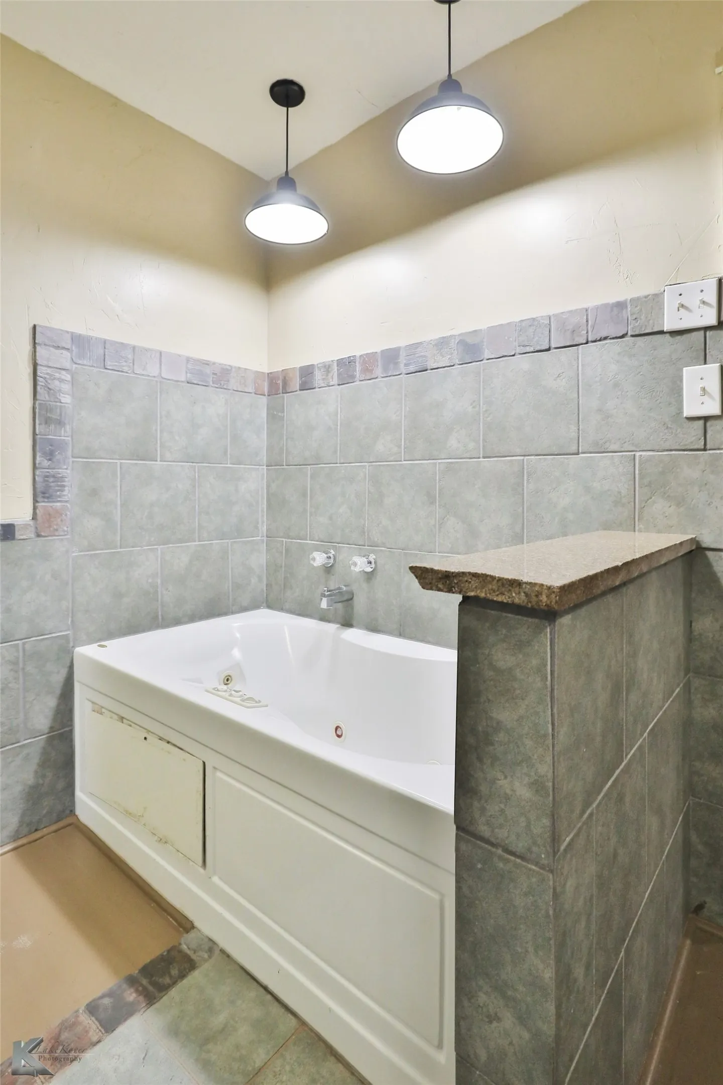 Spa-inspired primary bathroom featuring a freestanding soaking tub with chrome fixtures, soft-close cabinetry with wood-finish detailing, subway tile surround with contrasting border accent, pendant lighting, and polished concrete accent wall with integrated shelving