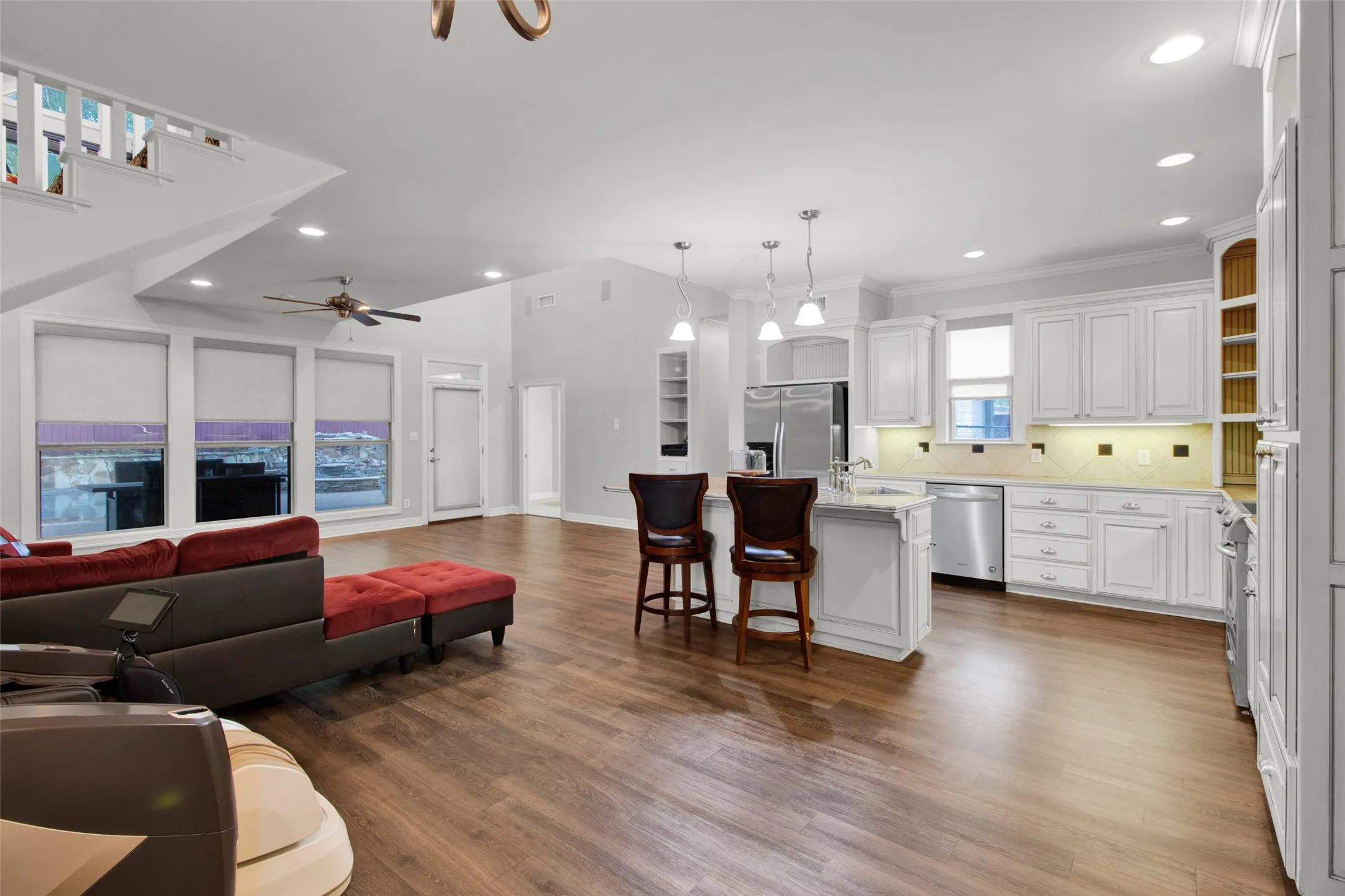 Open-concept living area featuring wood-finish flooring, a contemporary kitchen with white cabinetry, stainless steel appliances, and an island with counter seating