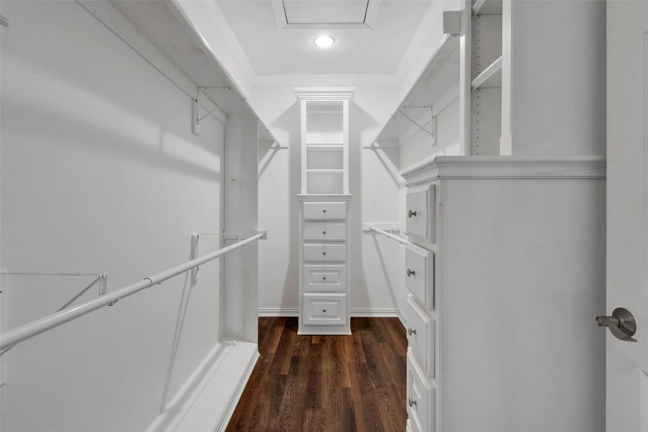 Walk-in closet featuring built-in shelving, hanging rods, central built-in storage with drawers and open shelving, wood-finish flooring, and recessed lighting