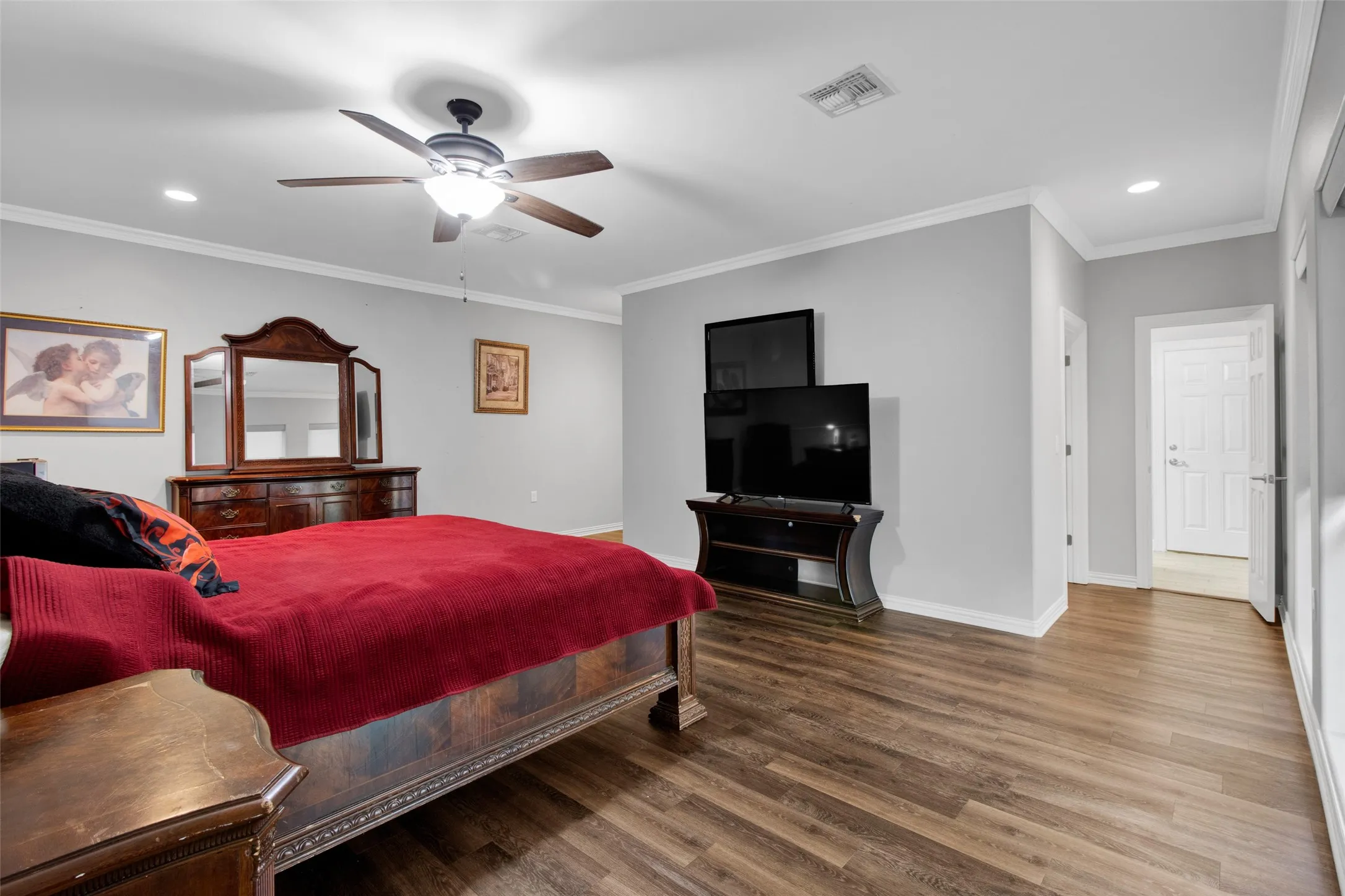Spacious room featuring wood-finish flooring, light gray walls, and white crown molding
