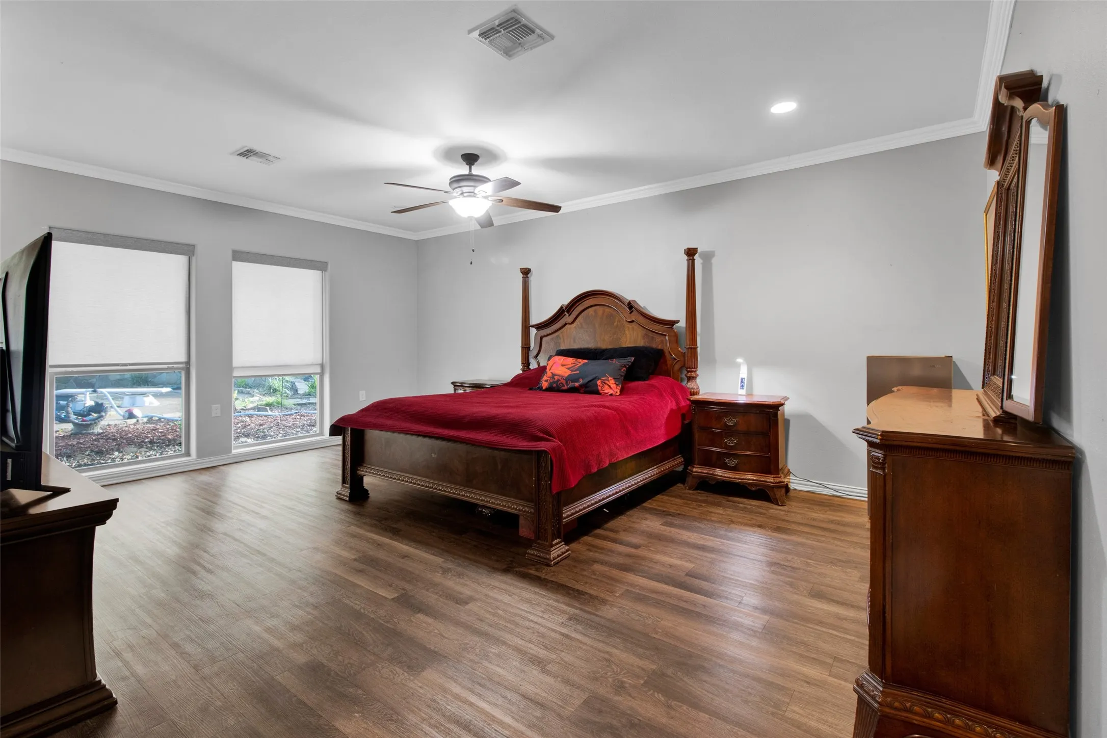 Spacious room featuring wood-finish flooring, two large windows, a ceiling fan with integrated lighting, recessed lighting, and crown molding