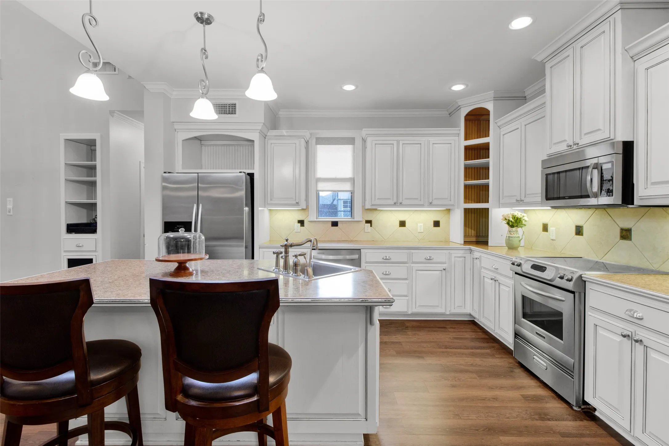 Spacious kitchen featuring an island with counter seating, extensive white cabinetry, stainless steel appliances, wood-finish flooring, and recessed lighting