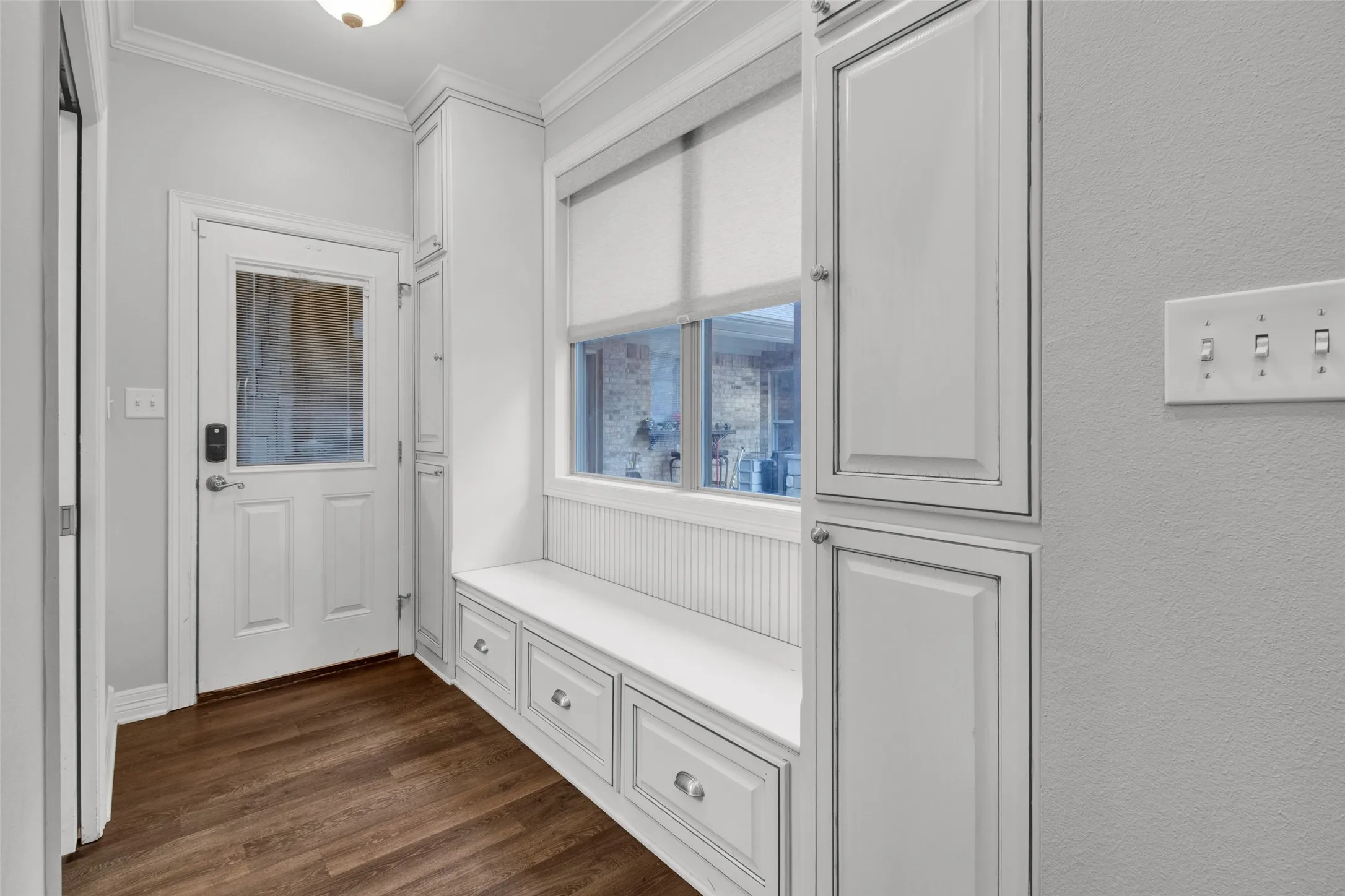 Entryway featuring wood-finish flooring, a white built-in bench with storage drawers, adjacent tall white cabinetry, and a glass-paneled exterior door
