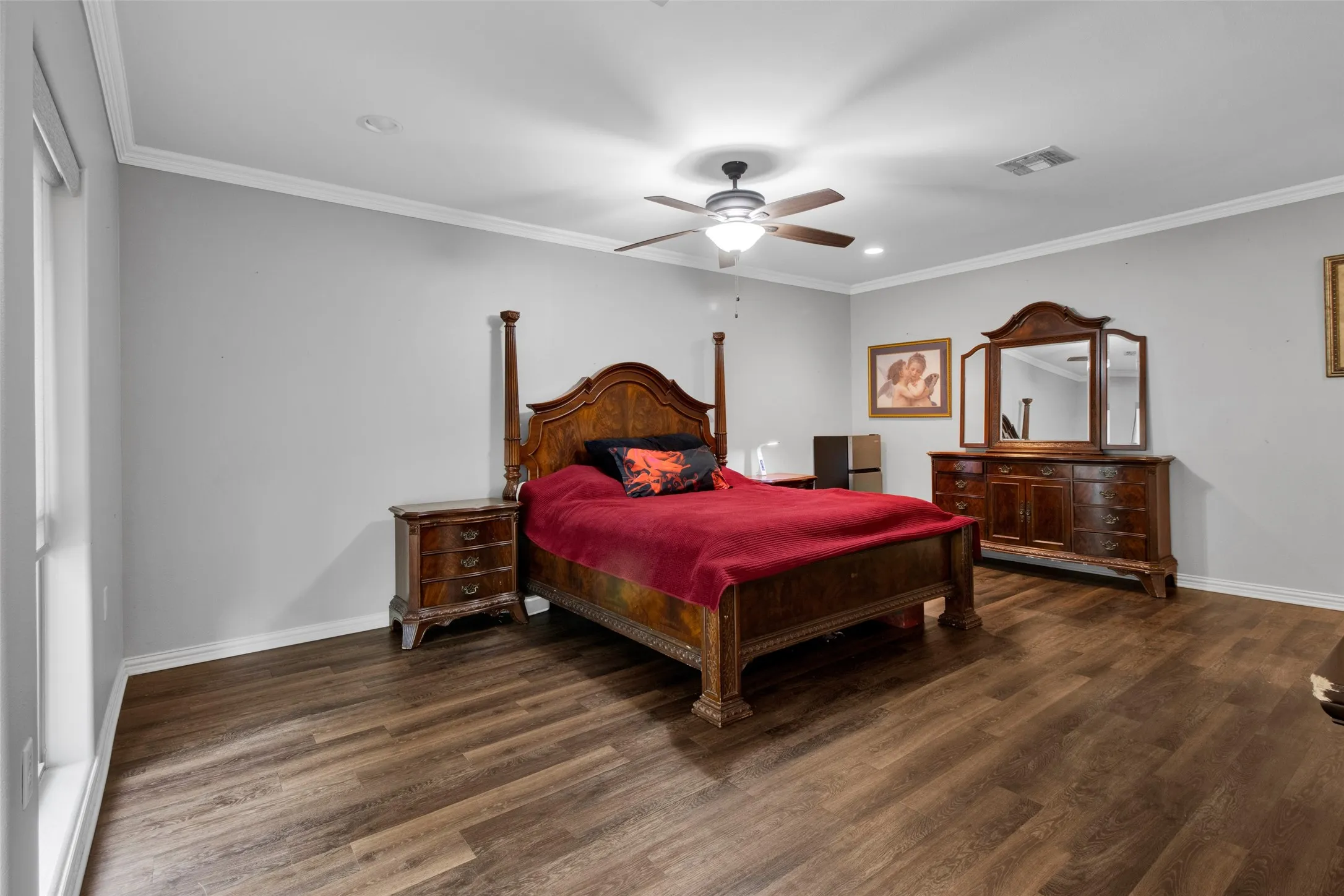 Spacious room featuring wood-finish flooring, white baseboards, and crown molding
