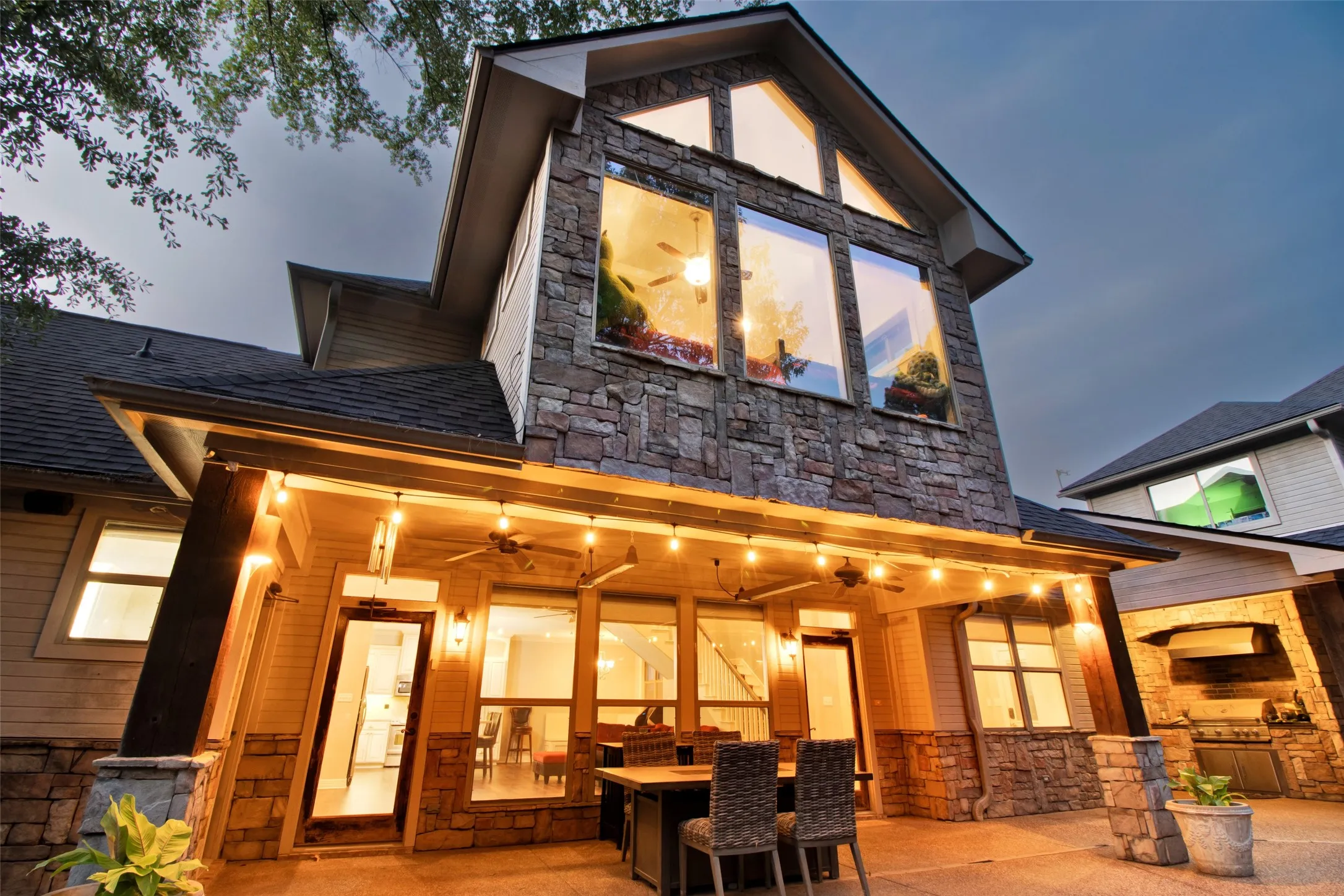 Stone and siding exterior featuring a covered patio, outdoor kitchen, and large windows