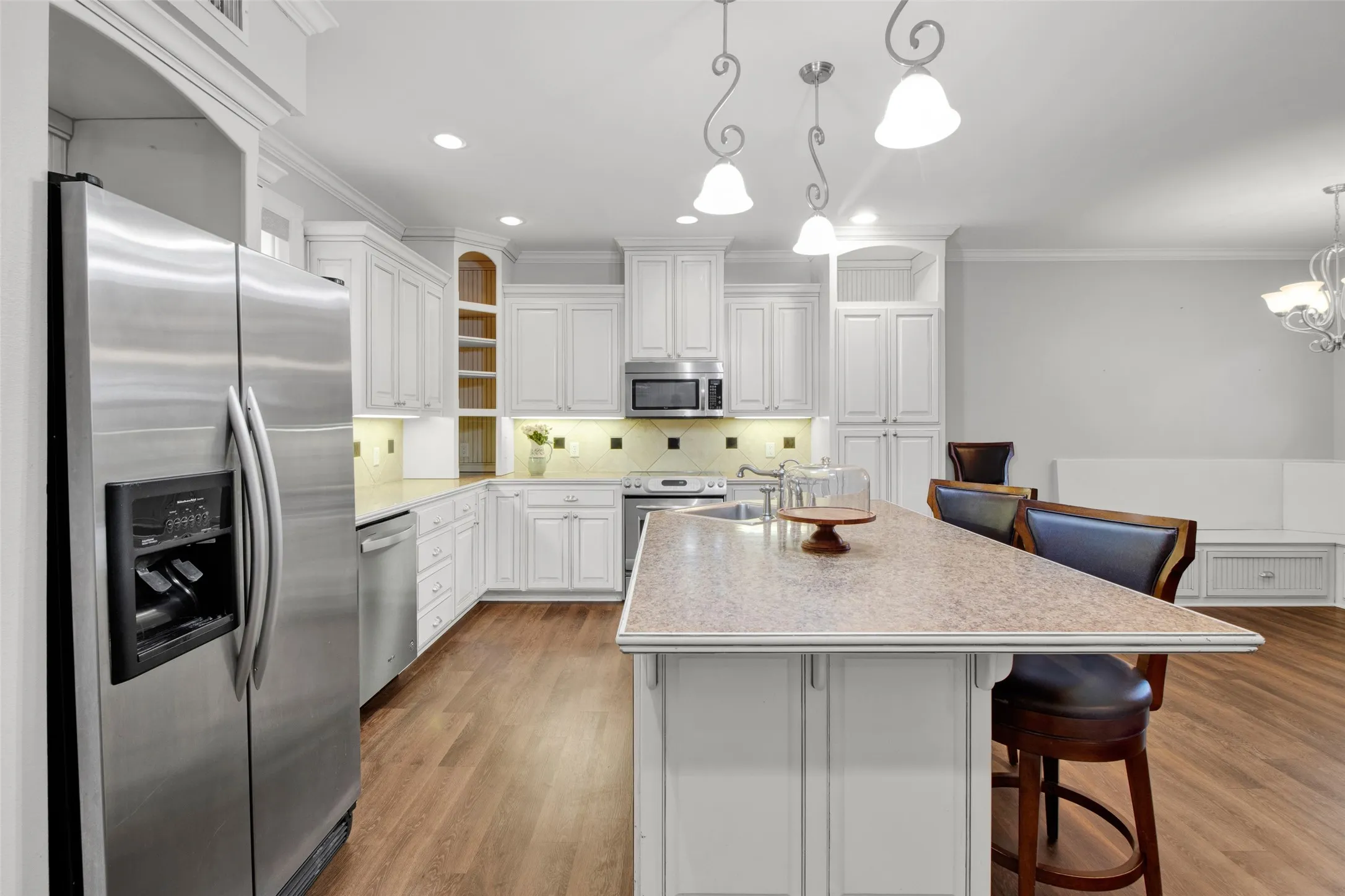 Spacious kitchen featuring white cabinetry, stainless steel appliances, wood-finish flooring, recessed lighting, and an expansive island with a light-toned countertop