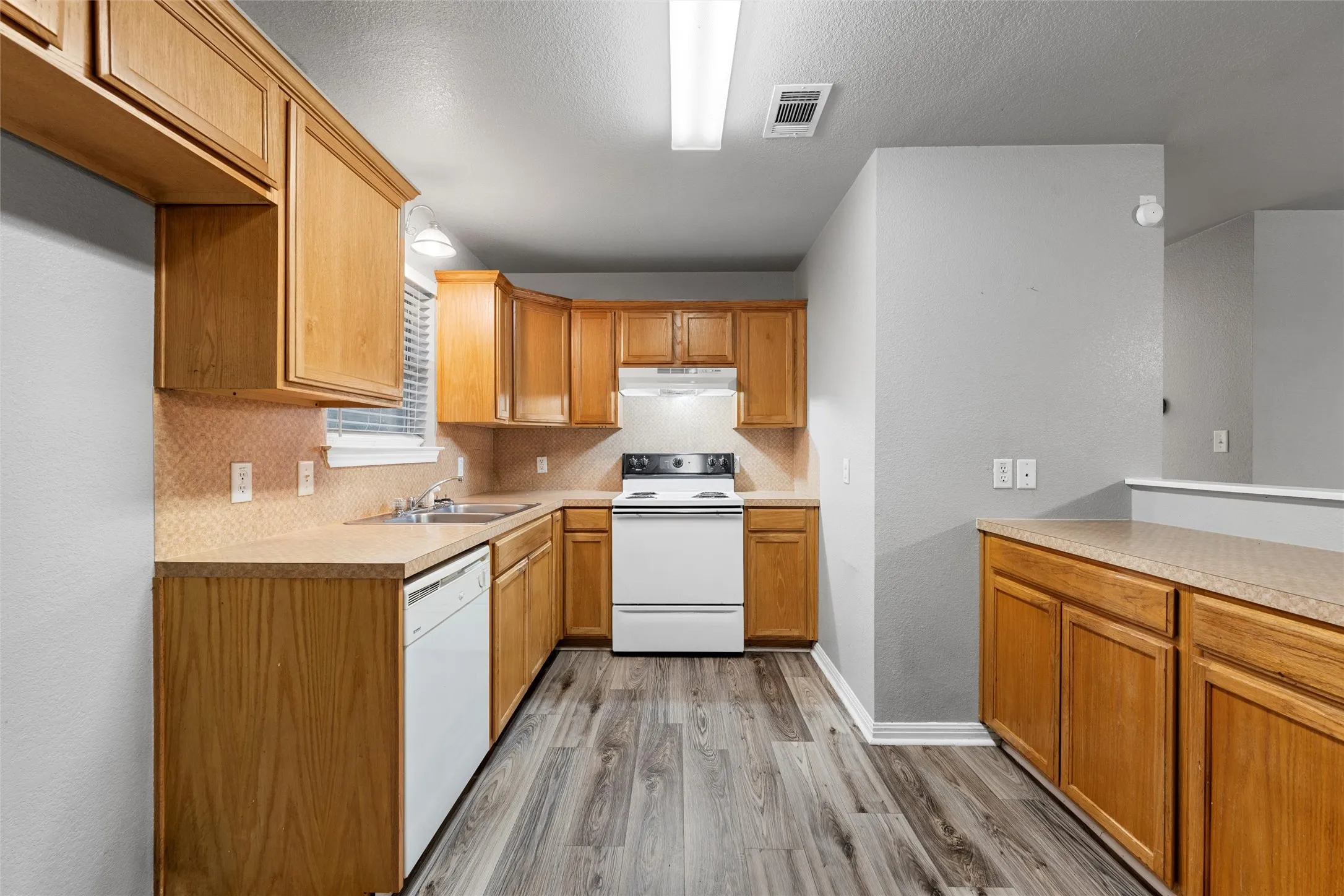 Kitchen with white appliances, under cabinet range hood, a sink, light wood-type flooring, and decorative backsplash
