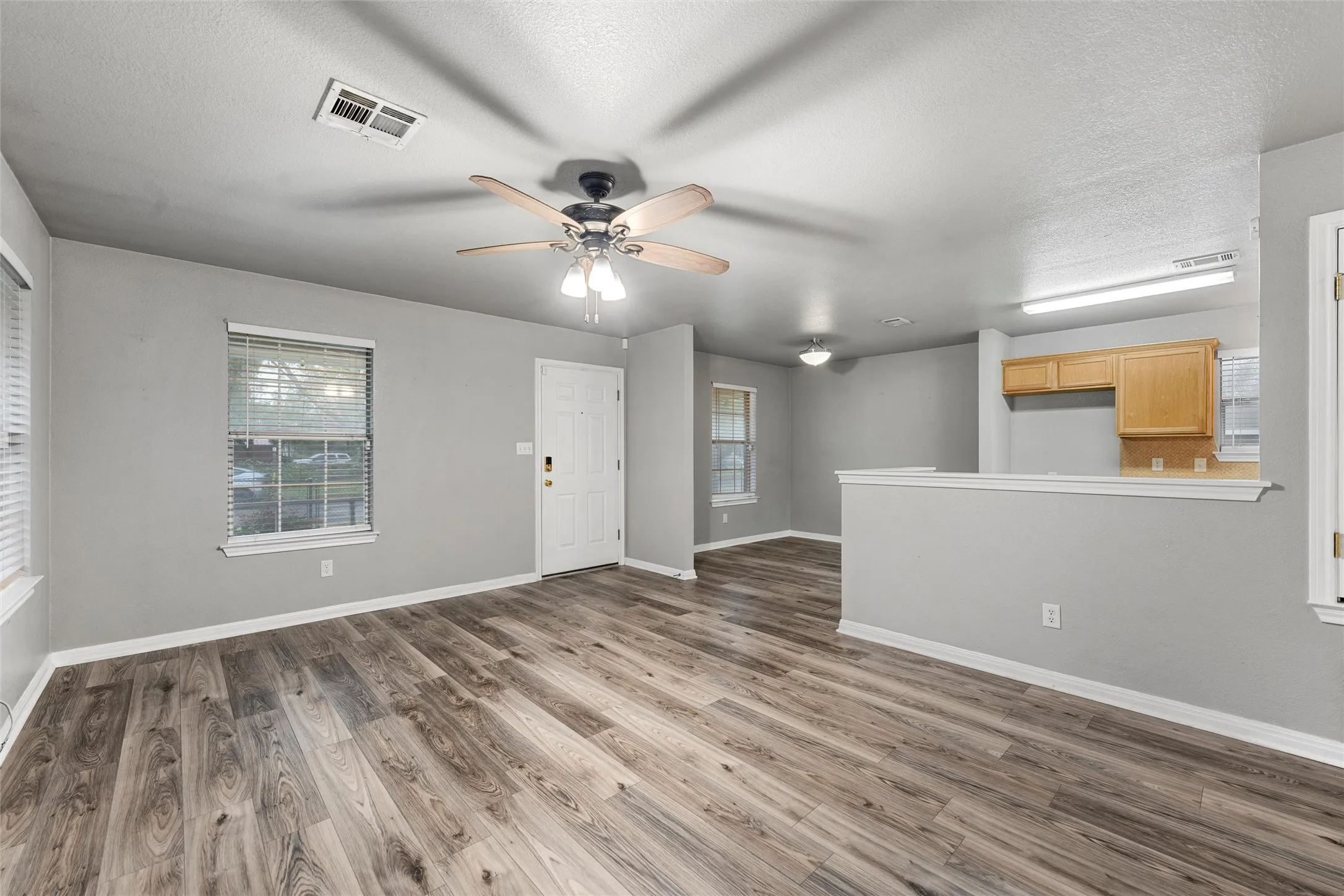 Unfurnished living room featuring plenty of natural light, a ceiling fan, wood finished floors, and a textured ceiling