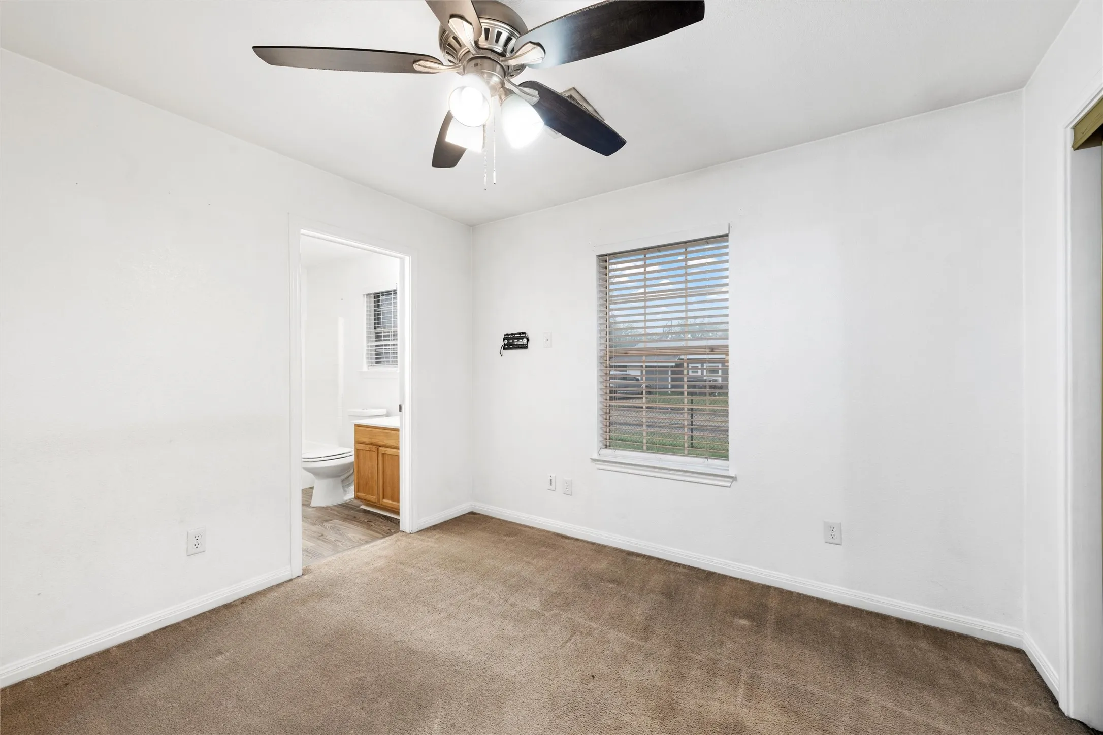 Unfurnished bedroom featuring light carpet, baseboards, connected bathroom, and a ceiling fan