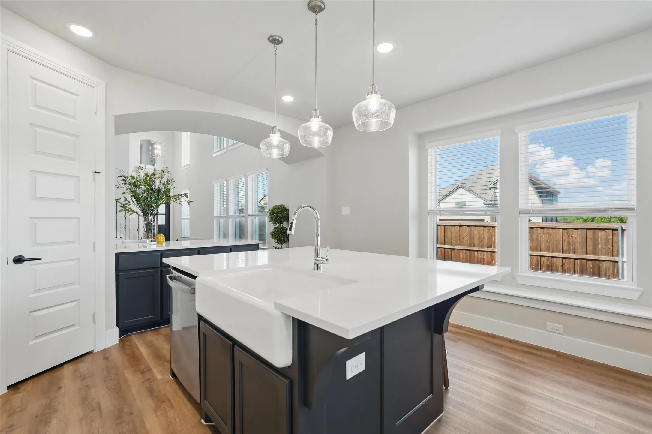 Contemporary kitchen featuring a black waterfall-edge island with an integrated apron-front sink, white quartz countertops, and polished wood-finish flooring