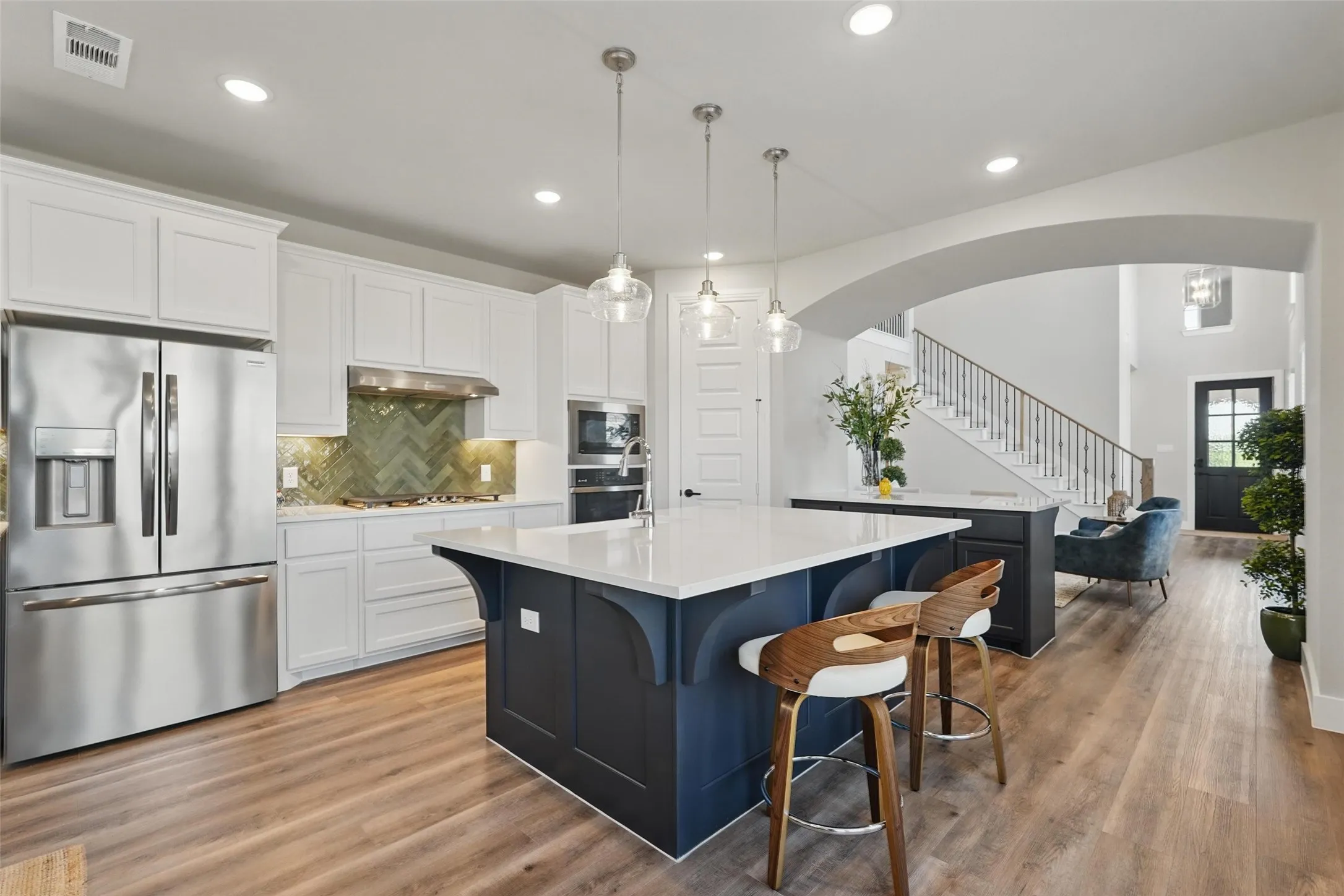 Kitchen featuring a stainless steel refrigerator, white cabinetry, a green herringbone tile backsplash, and two kitchen islands with solid surface countertops