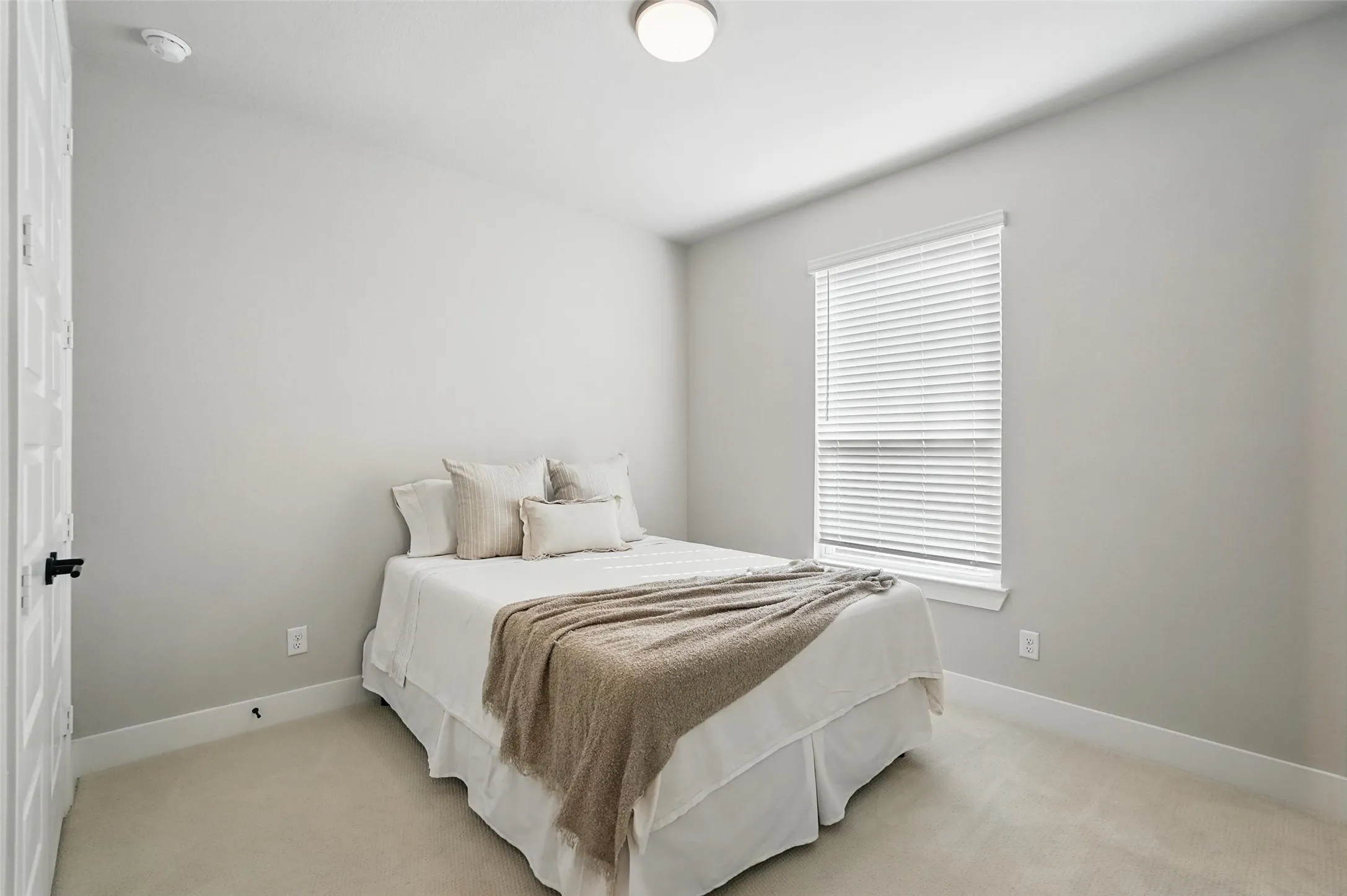 Bright secondary bedroom with neutral wall finishes, recessed ceiling lighting, and large window with horizontal blinds providing natural illumination and privacy control