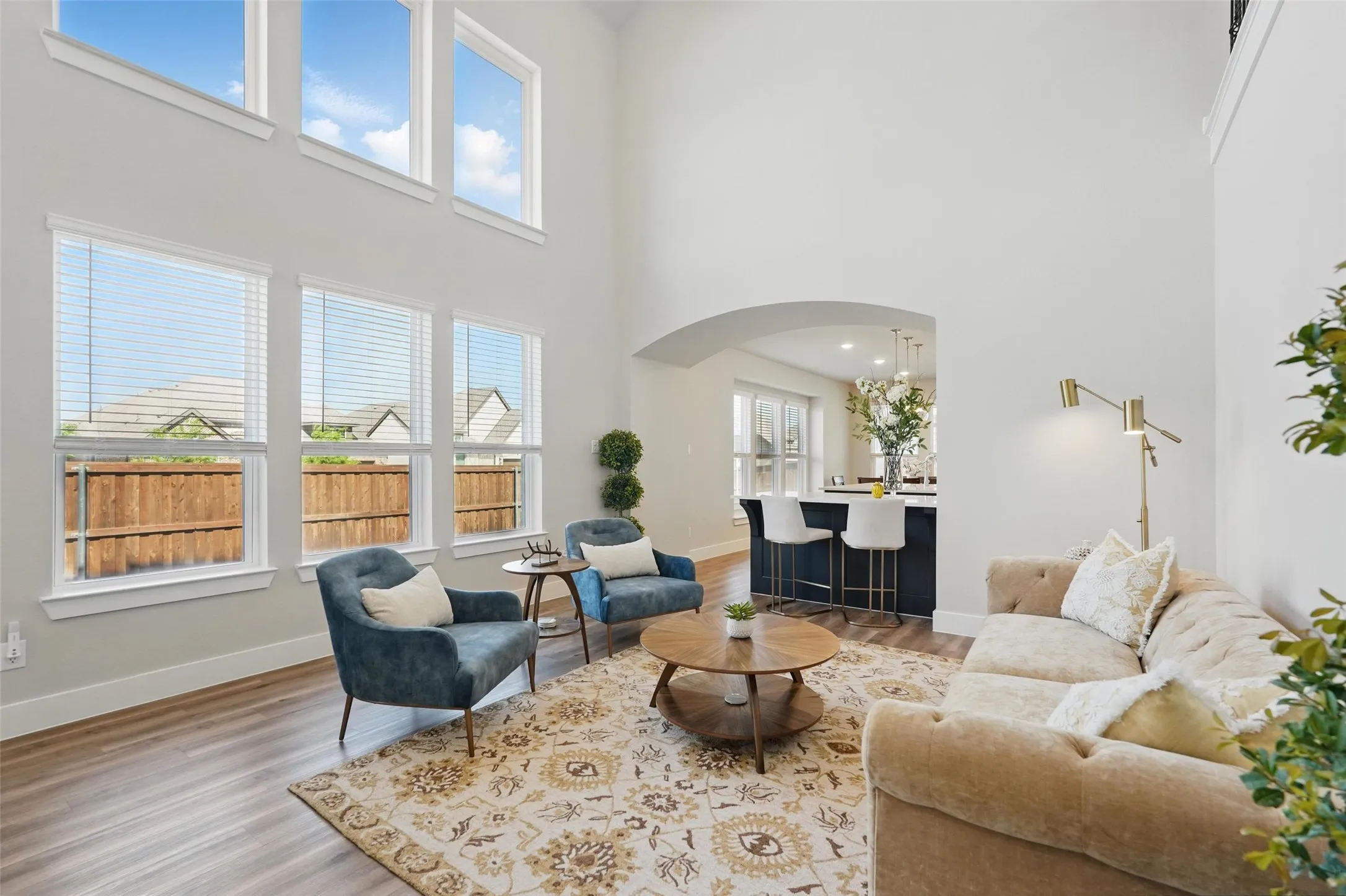 Soaring ceiling with high windows, wood-finish flooring, arched doorway, and an open-concept layout