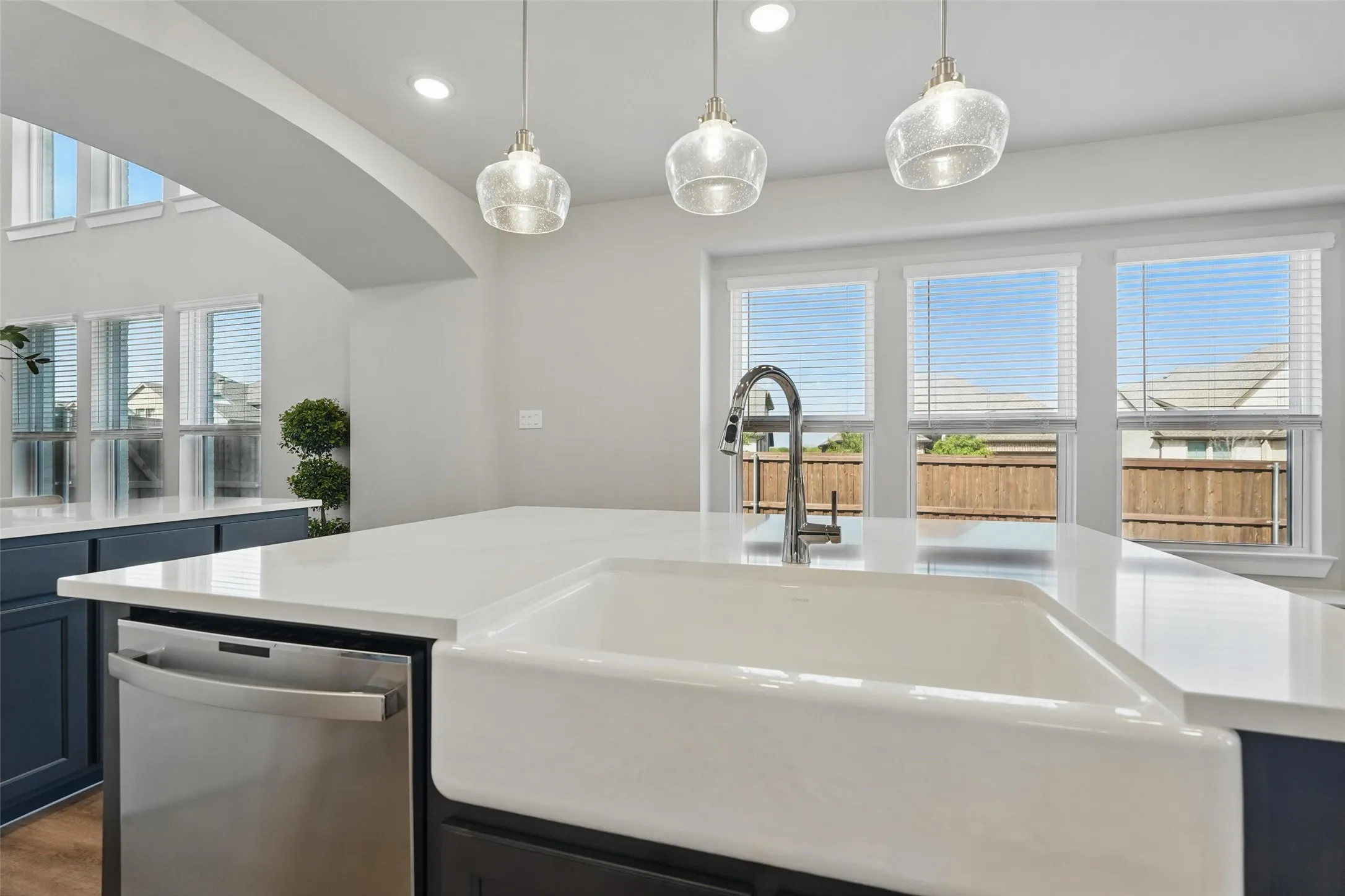 Gourmet kitchen featuring a large waterfall-edge quartz island with seating, stainless steel appliances, dark cabinetry, and pendant lighting