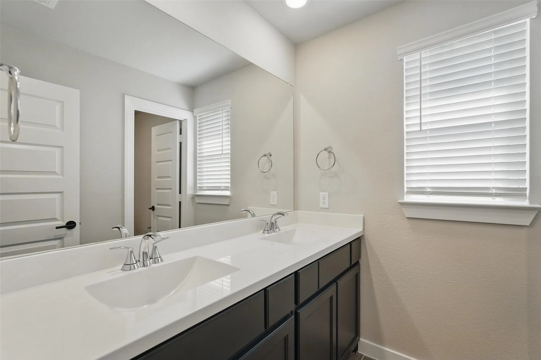 Dual-sink vanity with white quartz countertop, dark cabinetry, and polished chrome faucetry