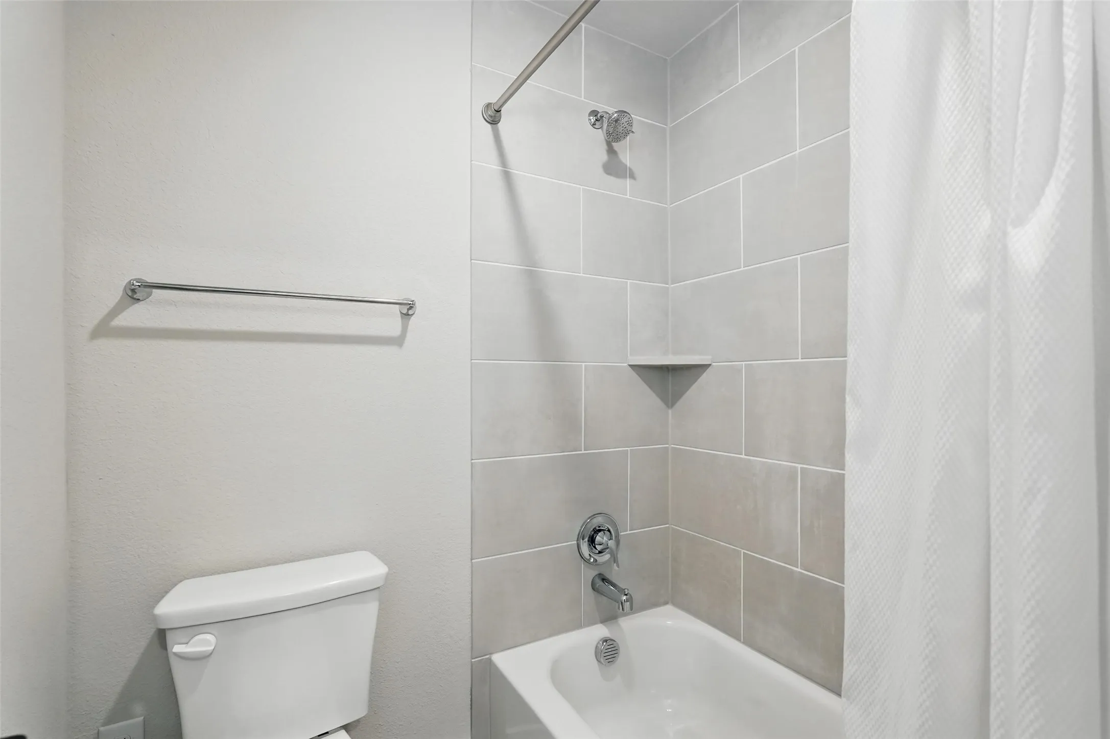 Clean and functional bathroom featuring subway tile walls, a ceramic bathtub with shower enclosure, chrome fixtures, and a toilet with tank