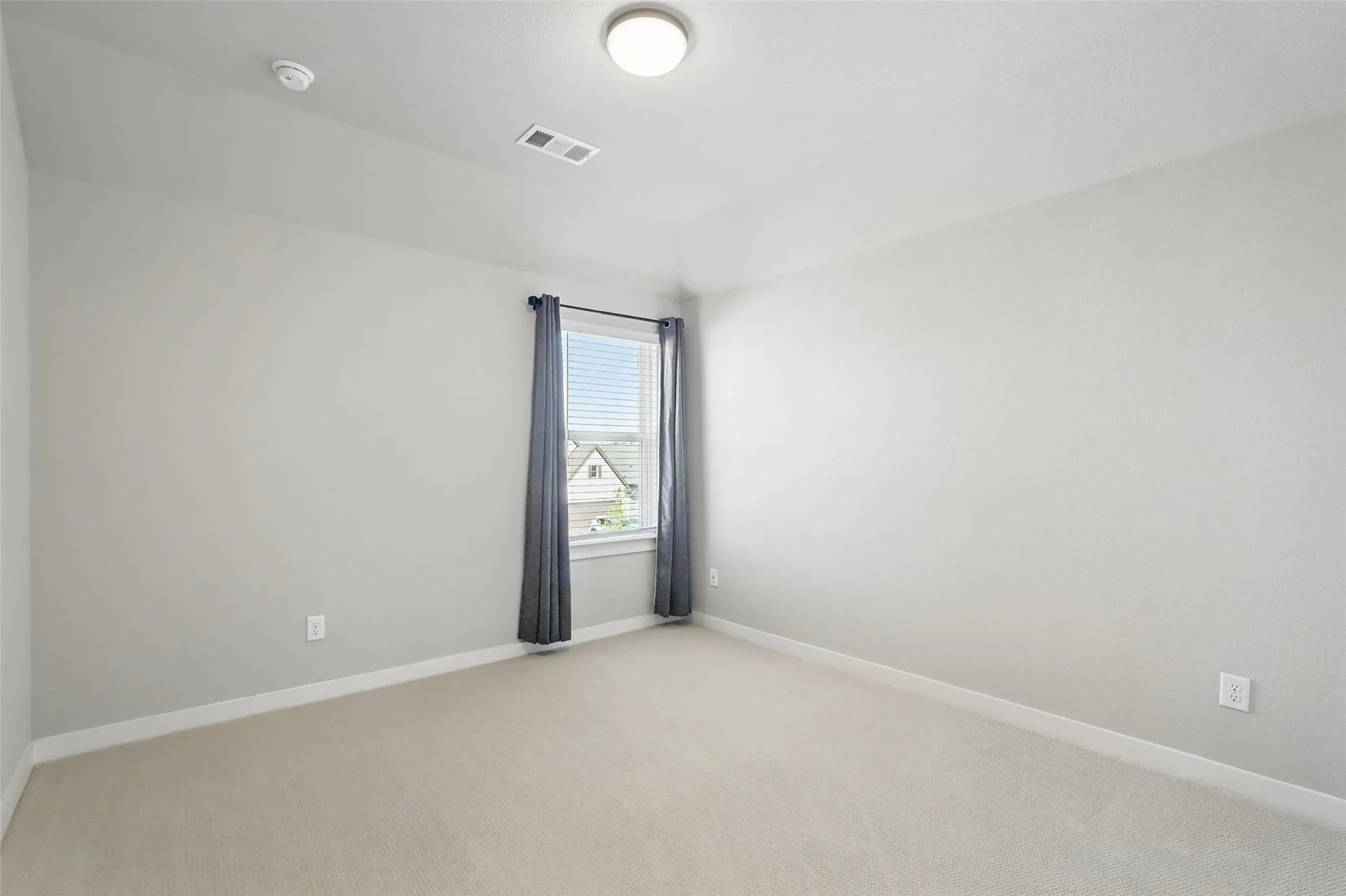 Bright secondary bedroom featuring neutral carpet flooring, recessed ceiling lighting, and a single window with plantation shutters and natural light exposure