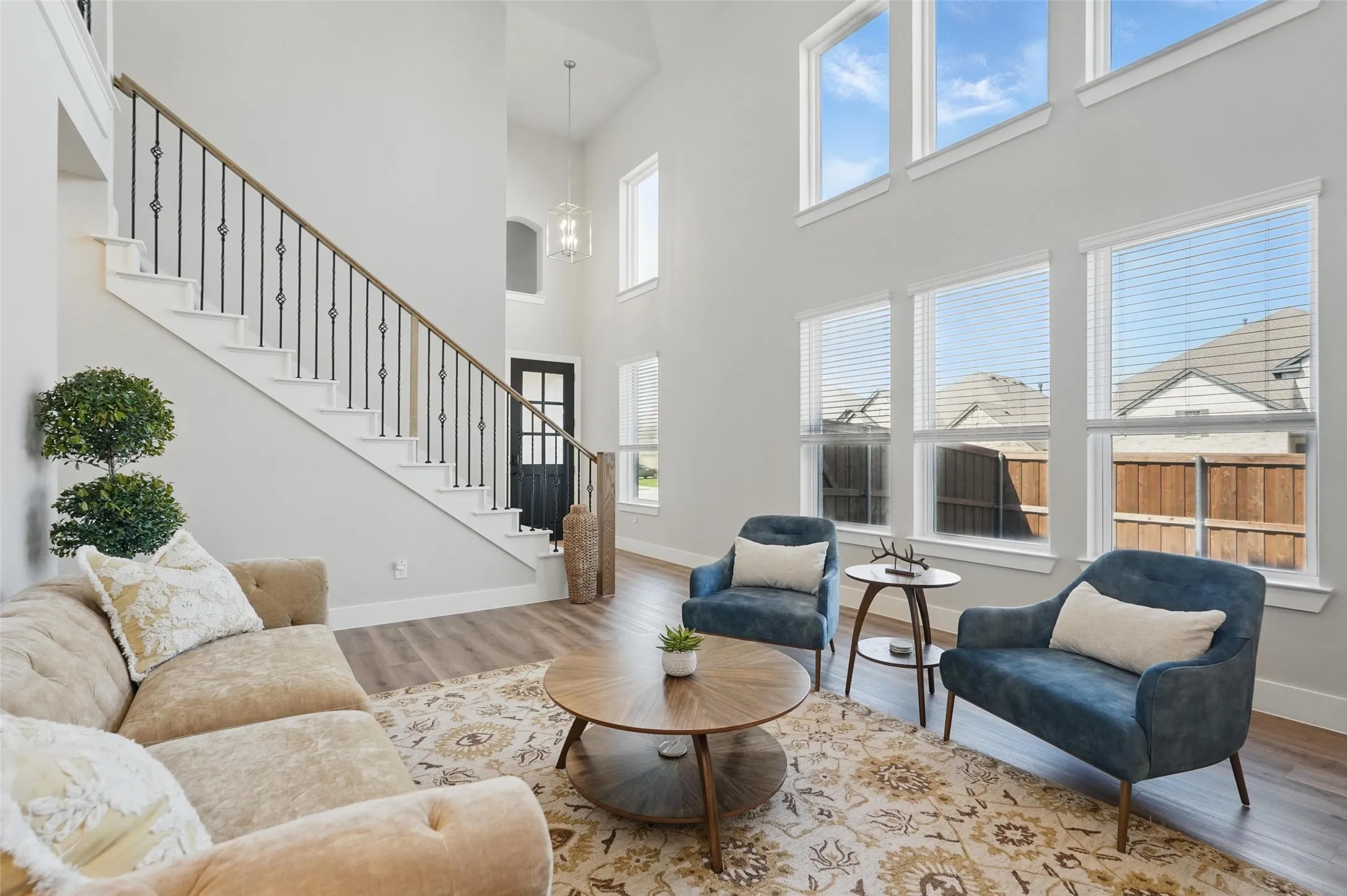 Vaulted ceiling with high windows, wood-finish flooring, staircase with wrought iron balusters, white trim, and a black paneled door