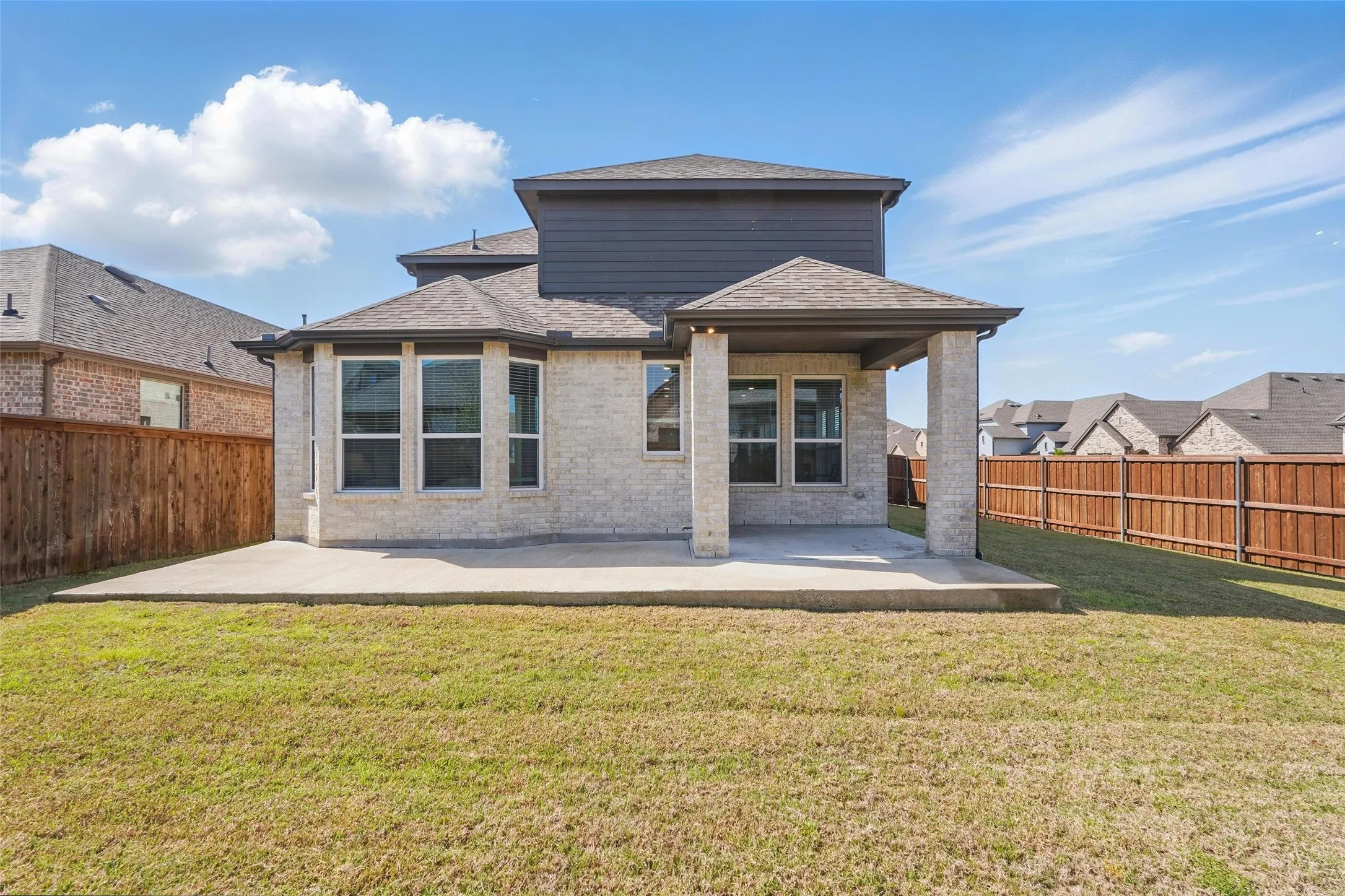 Expansive backyard featuring a covered patio, concrete patio, bay window, and privacy fencing