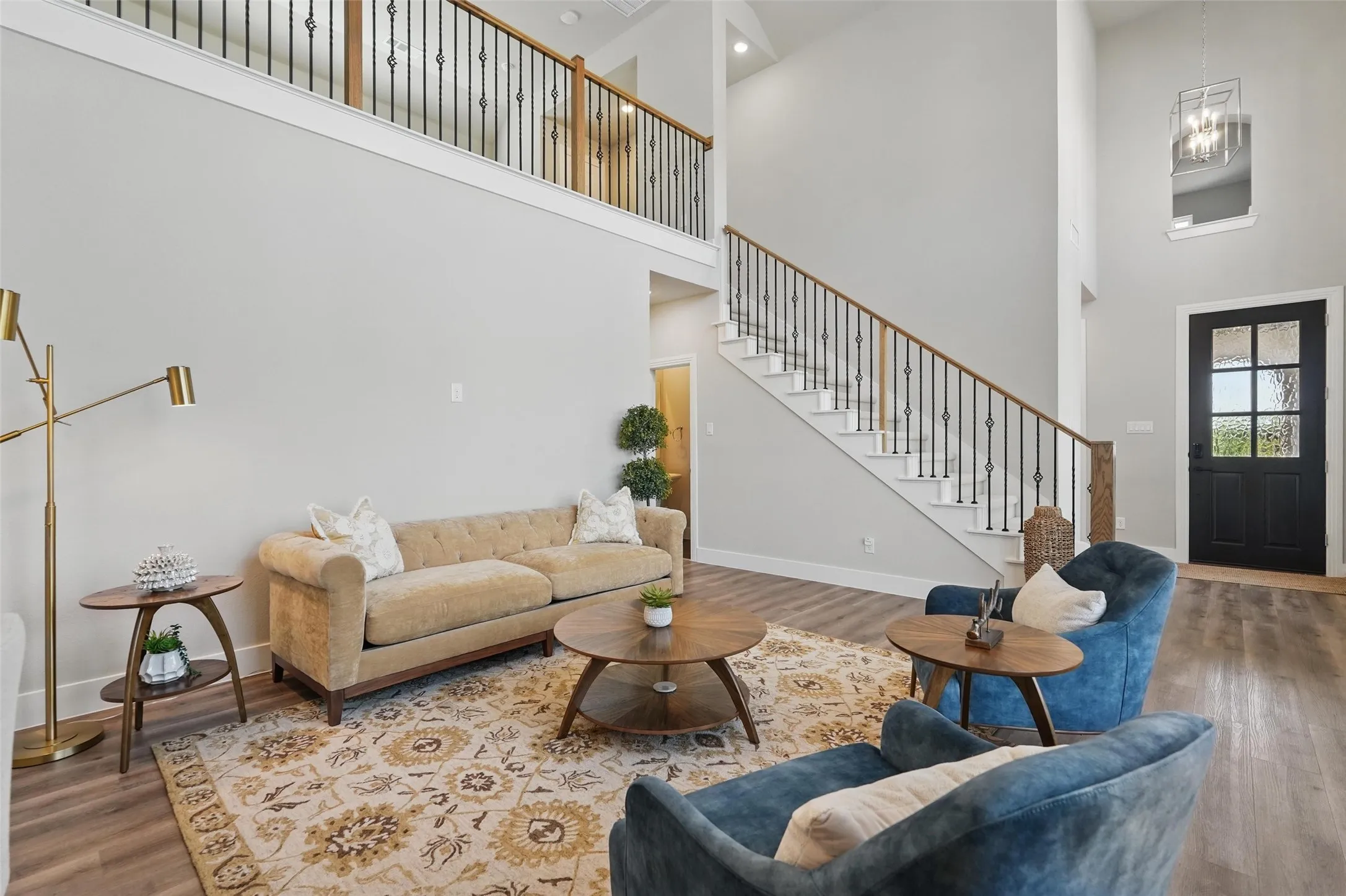 Soaring two-story living room with white walls, wood-finish flooring, and a floating staircase with metal railings