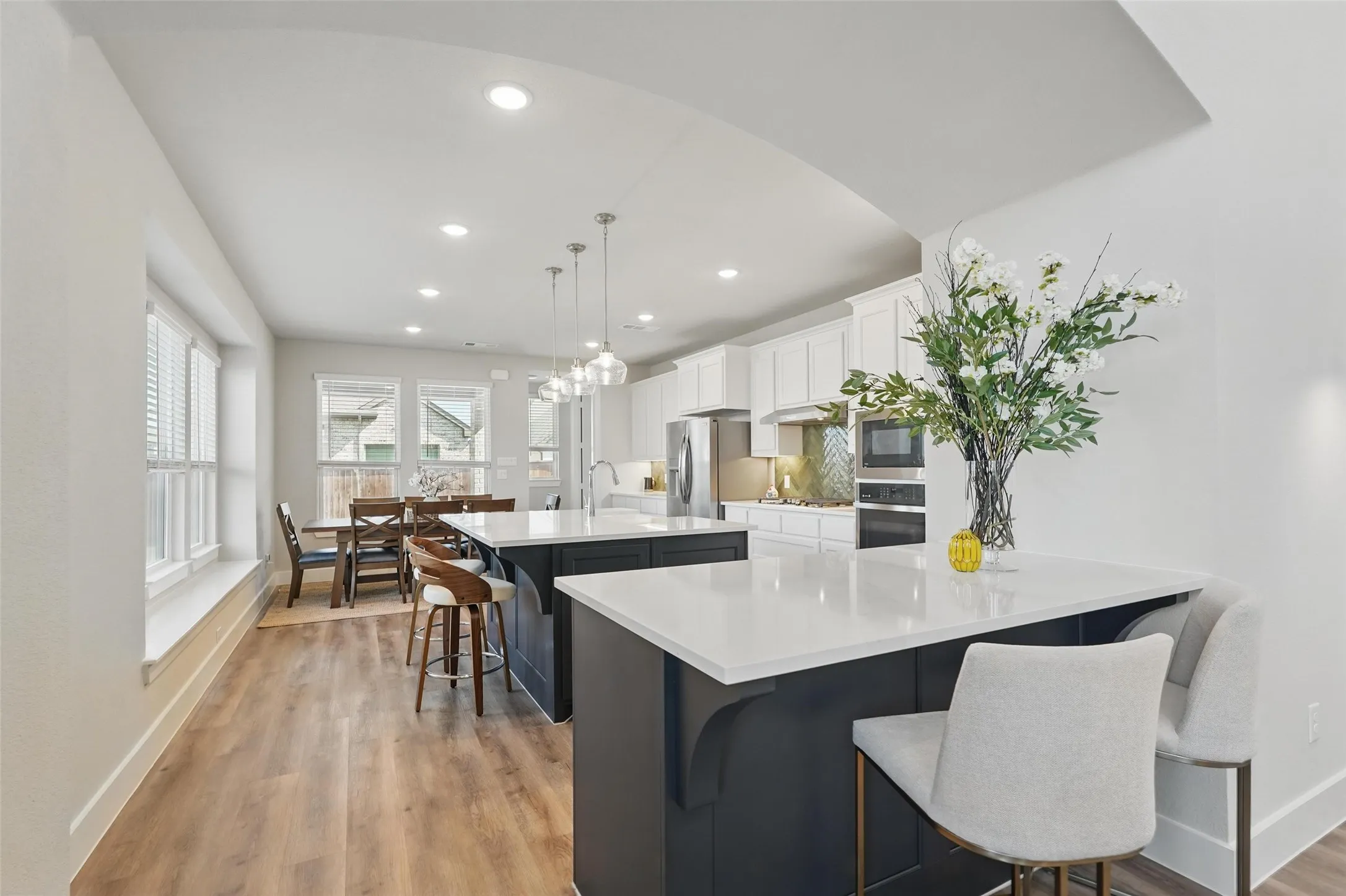 Open-concept kitchen and dining area featuring dual islands with white countertops, wood-finish flooring, white cabinetry, and recessed lighting