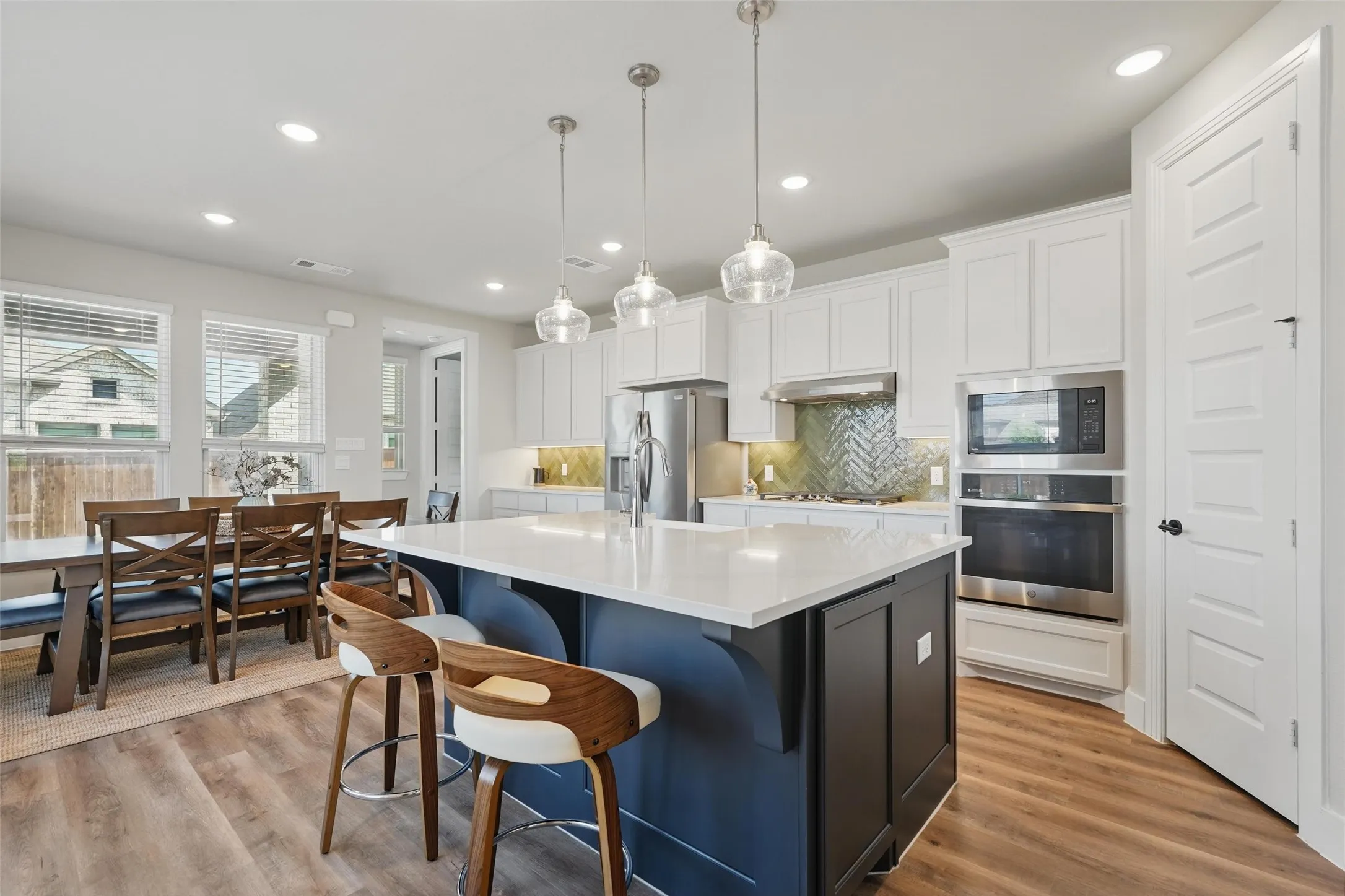 Open-concept kitchen featuring an island with a white countertop, built-in stainless steel appliances, white cabinetry, wood-finish flooring, and pendant lighting