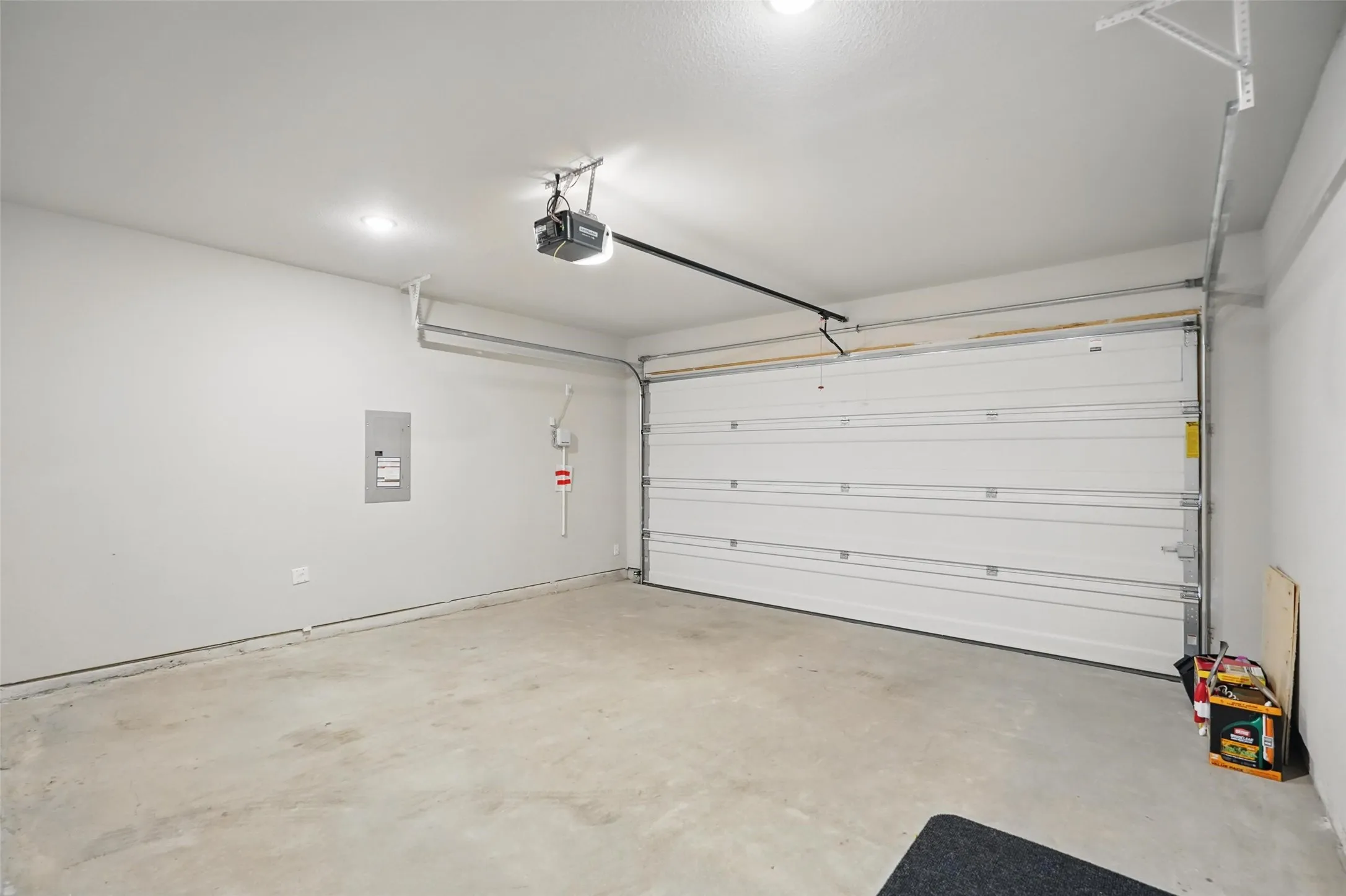 Concrete flooring, white walls, overhead lighting, automatic garage door opener, and a panel box