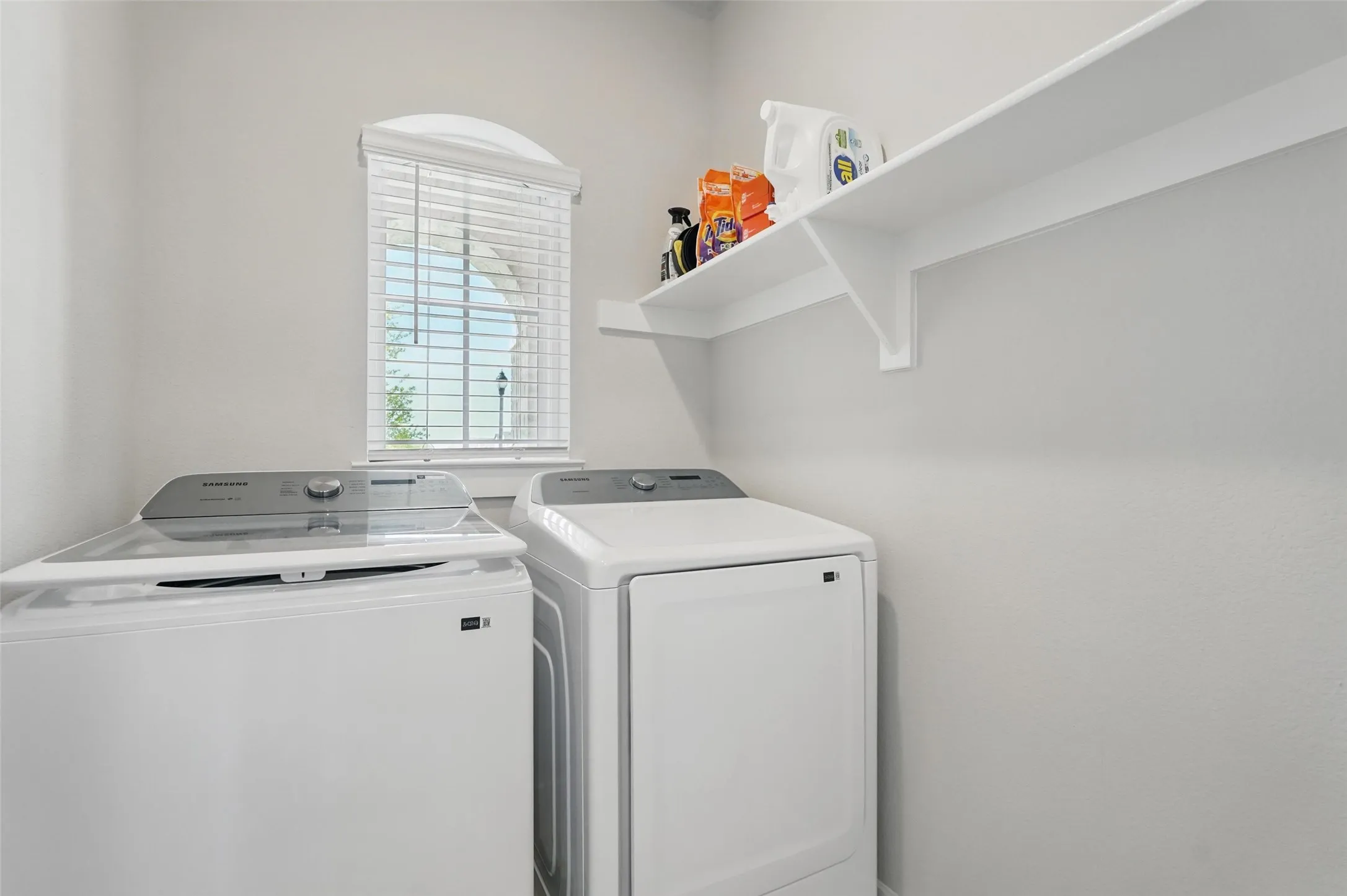 Arched window with blinds, white wall-mounted shelving, and white walls