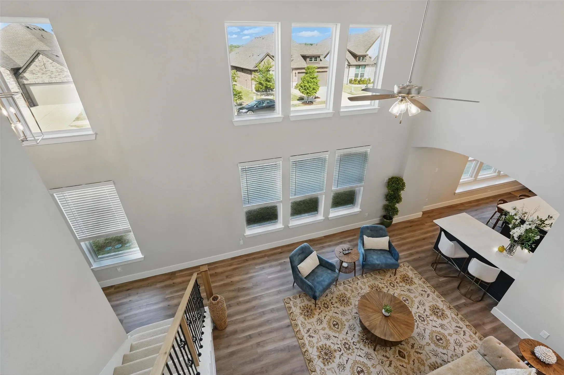 Two-story living area with high ceilings, multiple windows, wood-finish flooring, and a ceiling fan