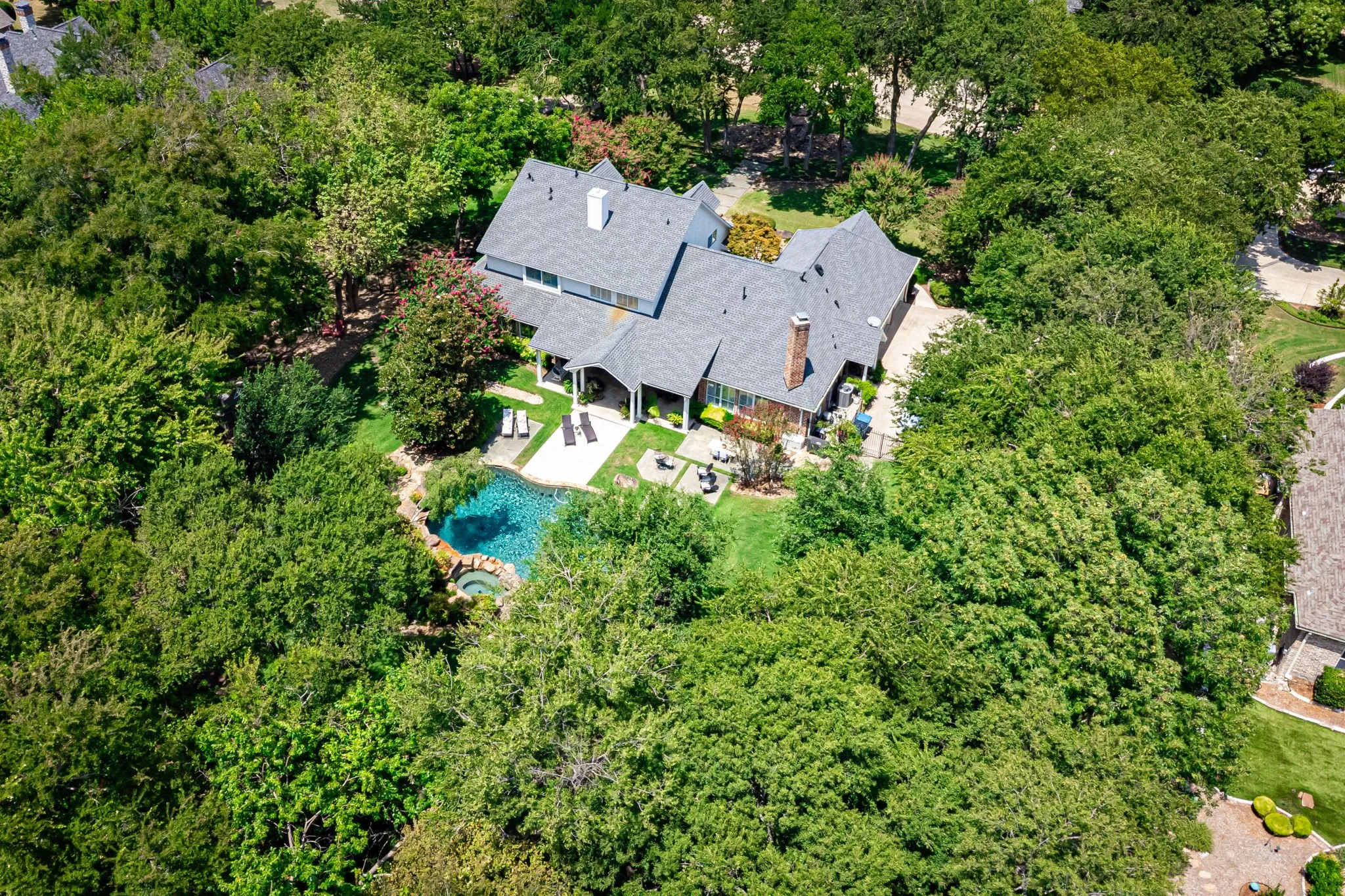 Mature landscaping surrounds the property, featuring a curved swimming pool and an integrated spa