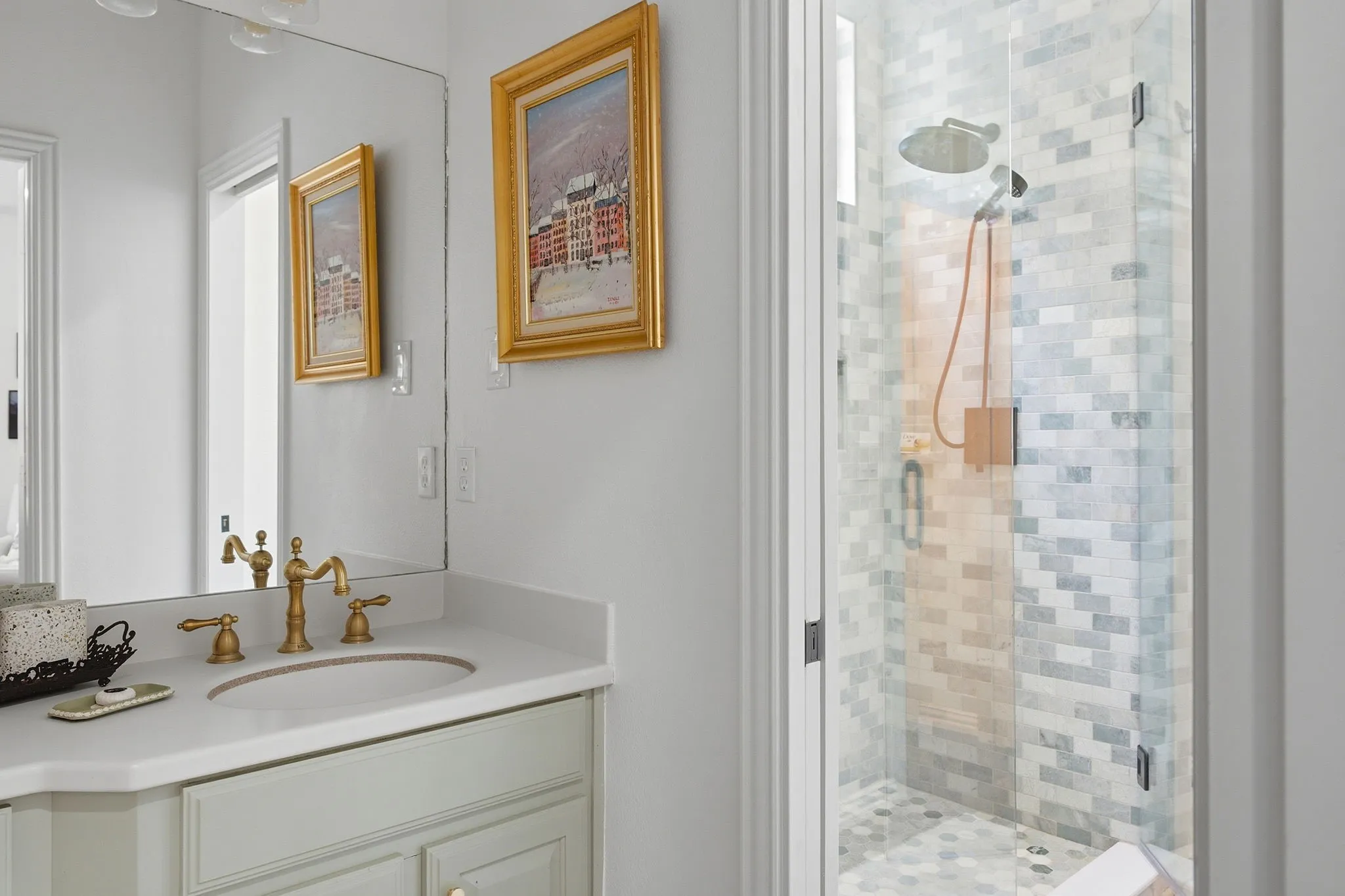 Elegant primary bathroom featuring a light-filled design with dual mirrors, brass-finished fixtures, and a white vanity with ample storage